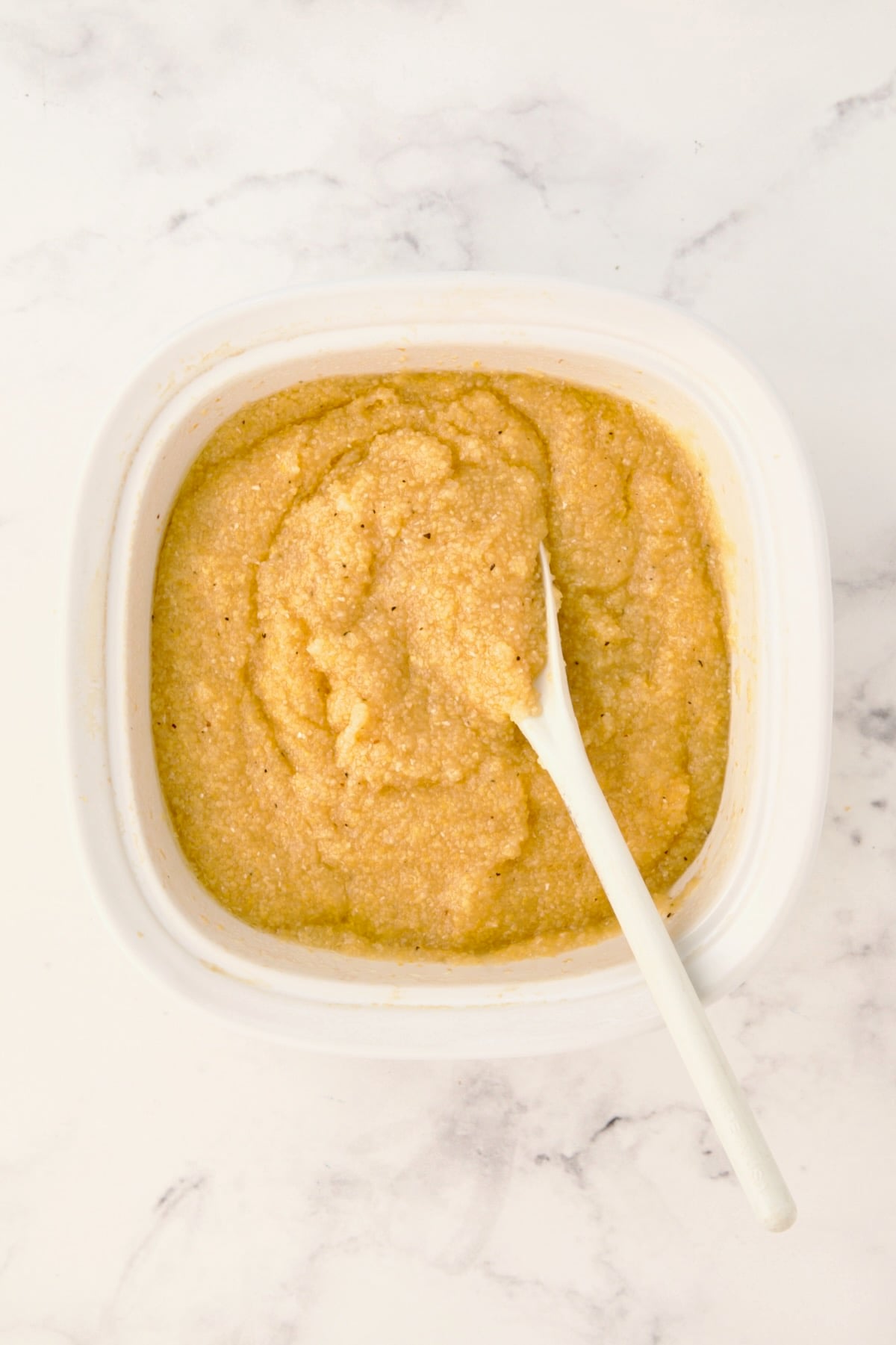 Cooked polenta in Corningware dish being mixed with white mixing spoon.