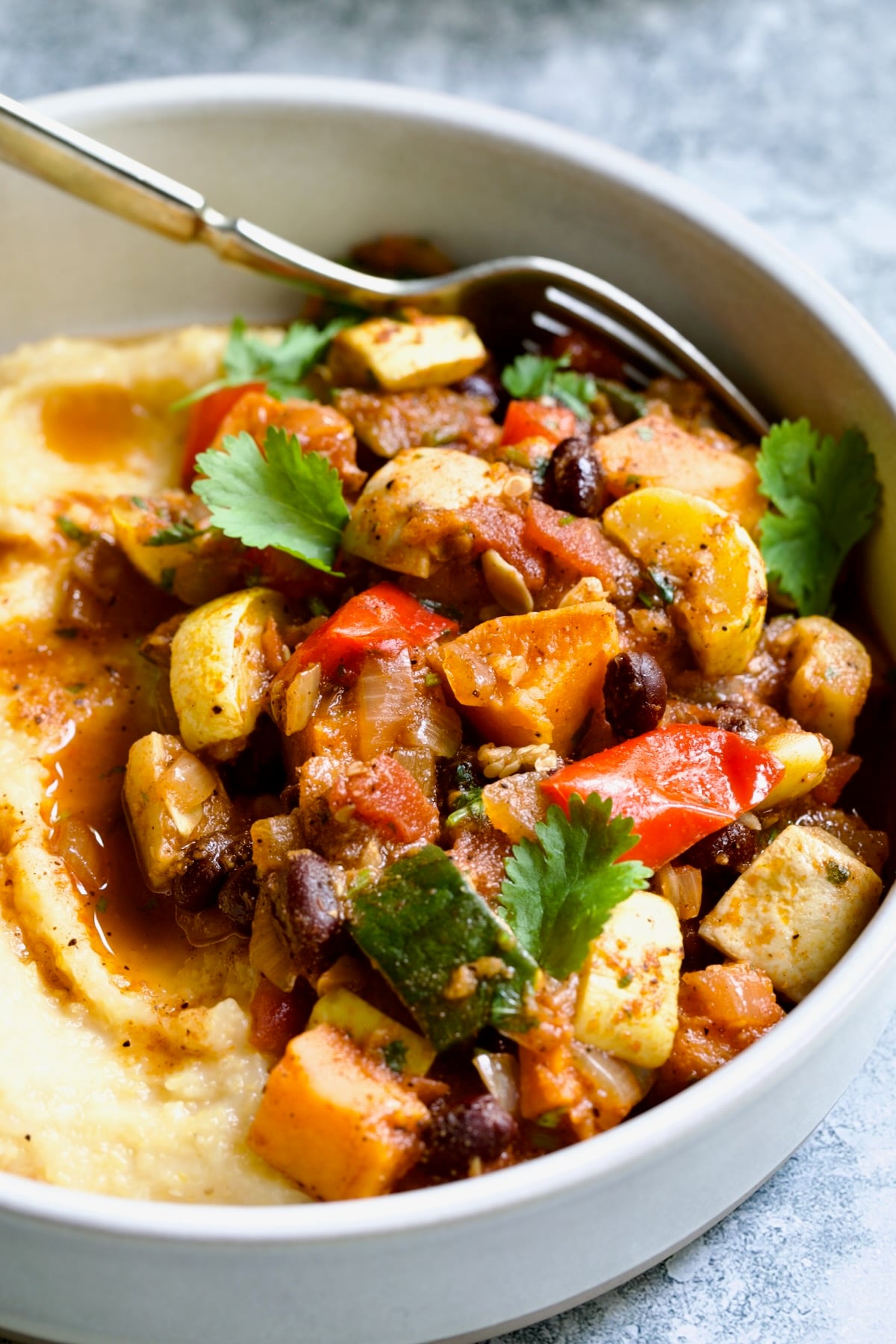 Roasted Vegetable Stew with Polenta in white bowl on blue napkin garnished with fresh cilantro leaves.