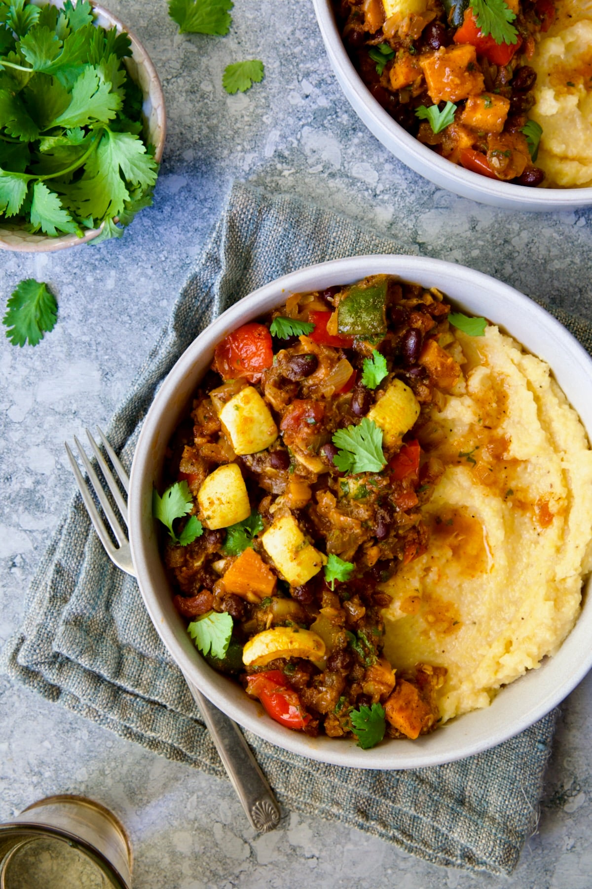 Roasted Vegetable Stew with Polenta in white bowl on blue napkin garnished with fresh cilantro leaves.