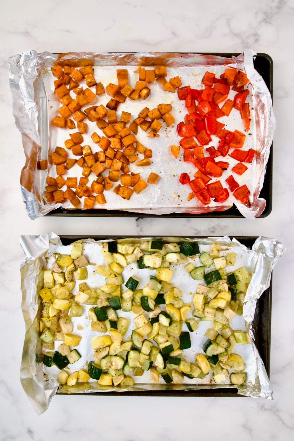 Cubed sweet potato, red bell pepper, yellow squash and zucchini on aluminum foil-lined rimmed sheet pans after being roasted.