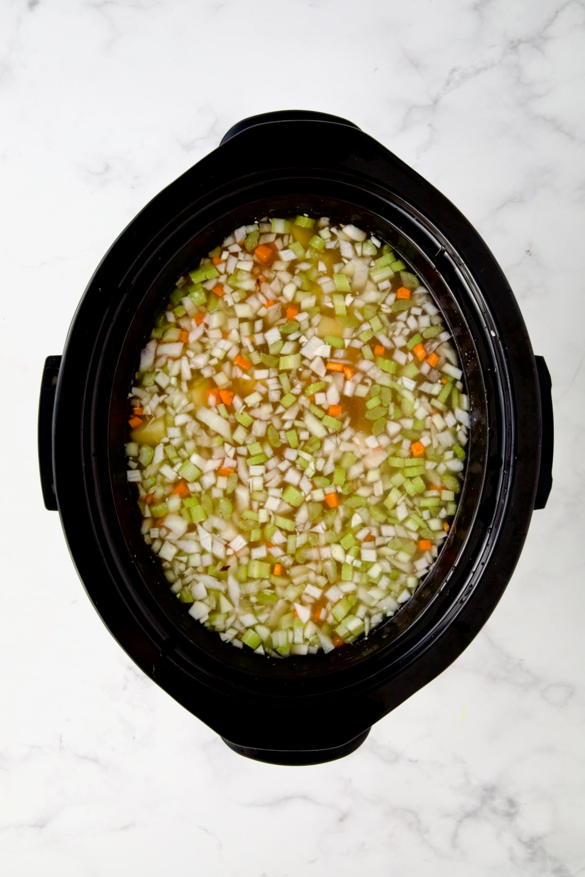 Diced vegetables and ham in black slow cooker before being mixed together with chicken broth added.