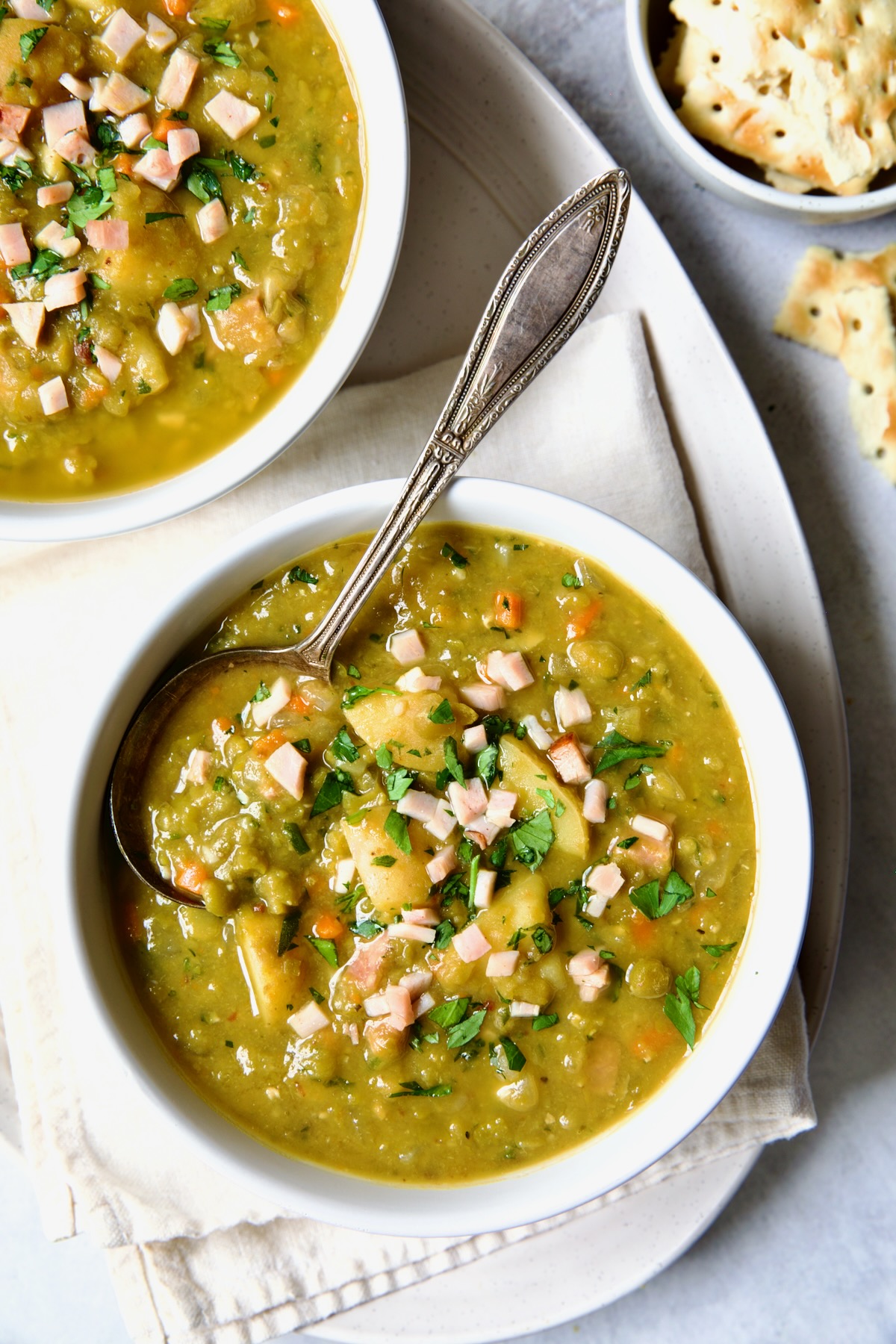 One serving of Slow Cooker Split Pea Soup in a white bowl on oval white platter.