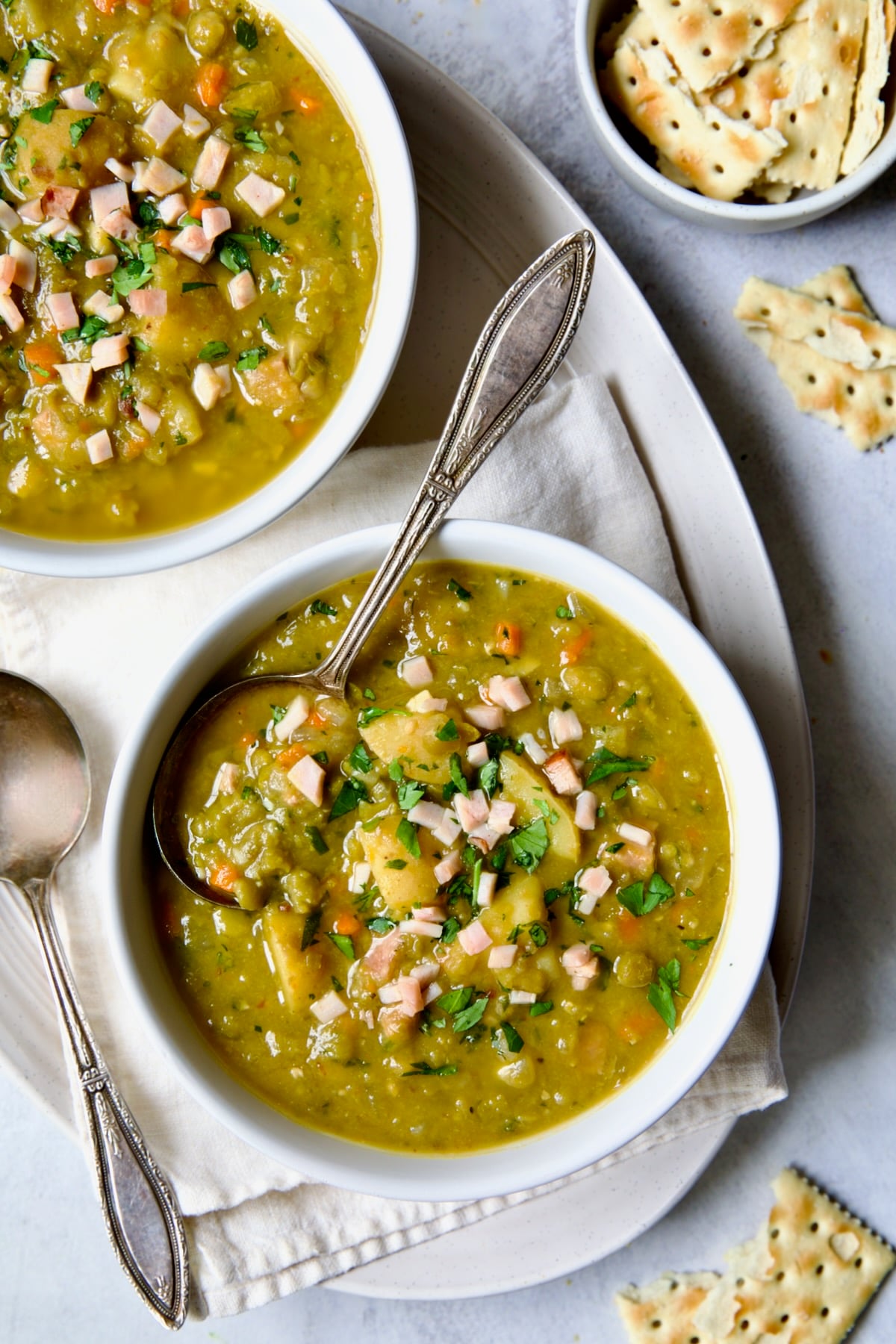 Two servings of Slow Cooker Split Pea Soup in white bowls on oval white platter.