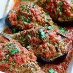 Four baked Stuffed Eggplant halves in white rectangular baking dish with serving spoon.