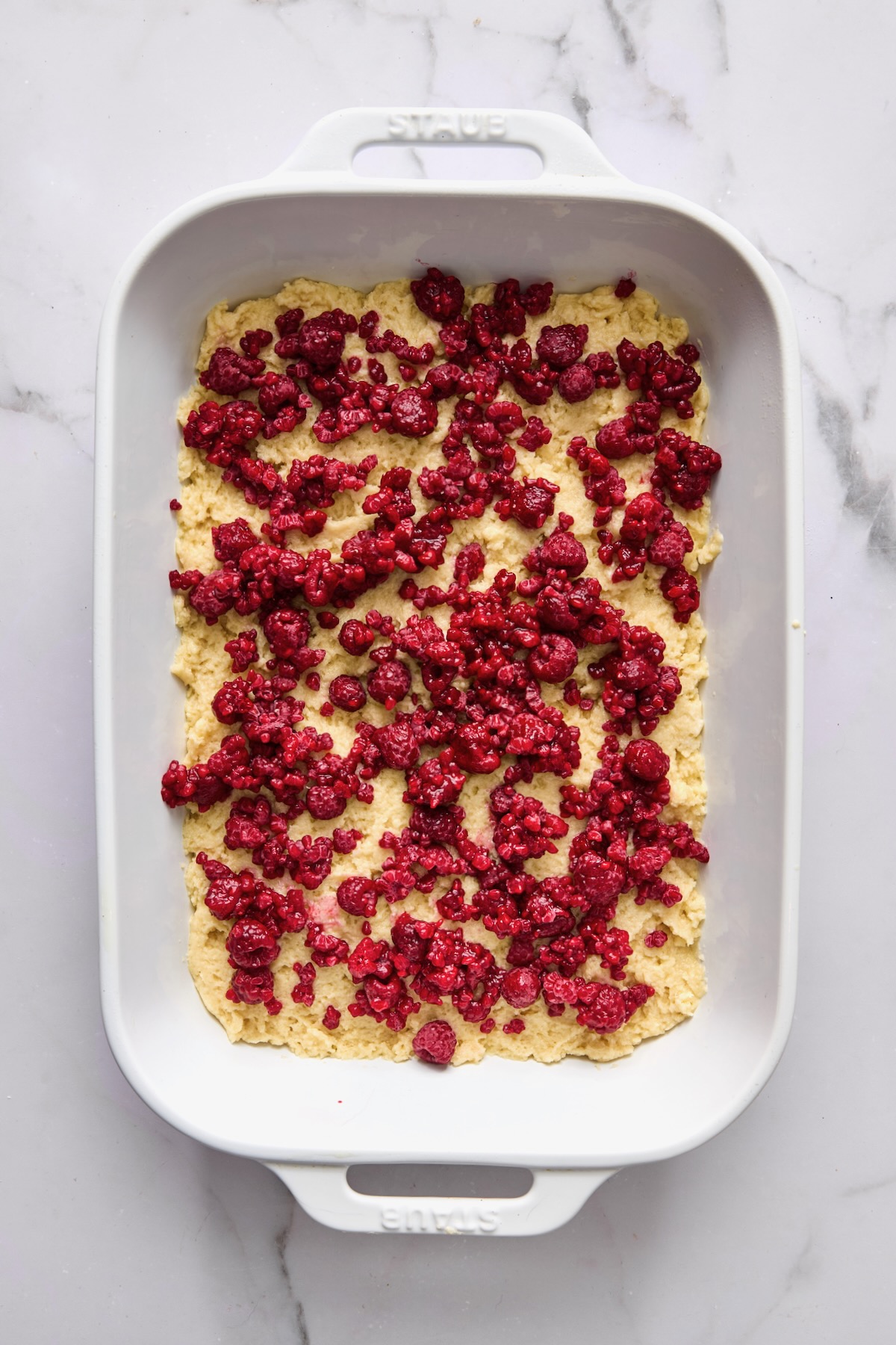 Drained frozen raspberries placed over batter for coffee cake in white rectangular baking dish.