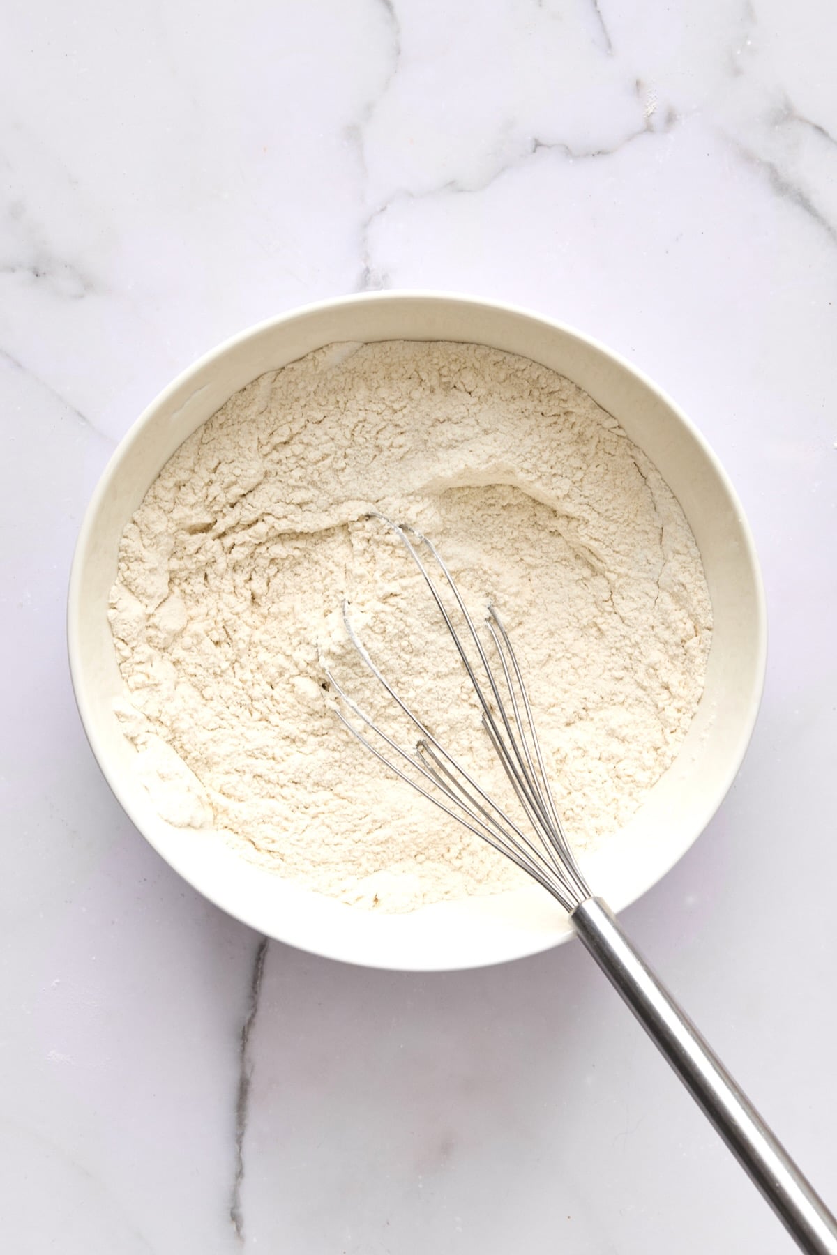 Dry ingredients for coffee cake mixed together in white bowl with wire whisk.