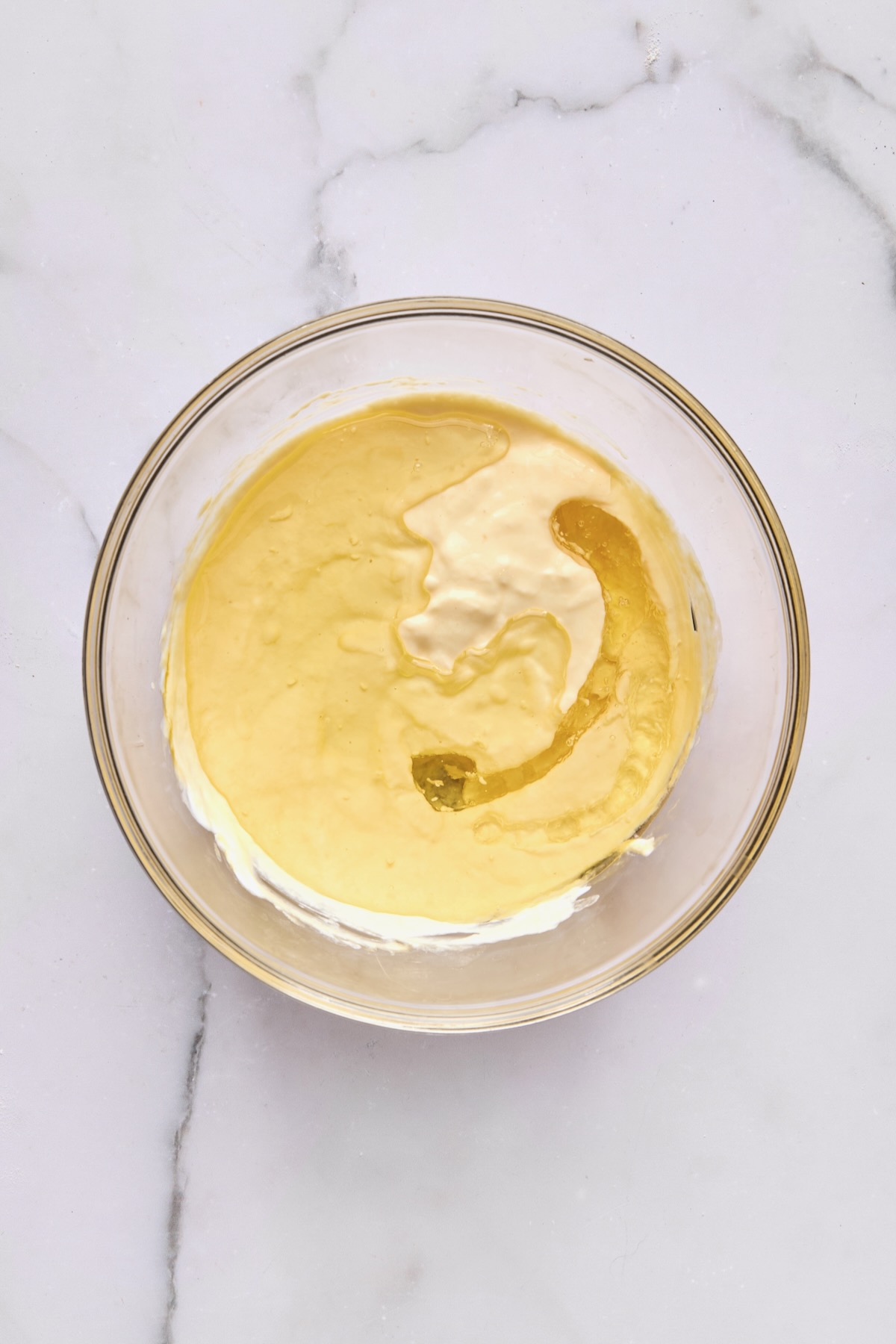 Wet ingredients for coffee cake in glass bowl with yogurt and oil added.