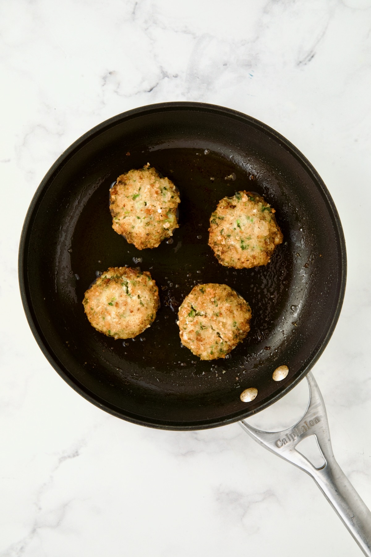 Four cooked shrimp cakes in nonstick skillet.