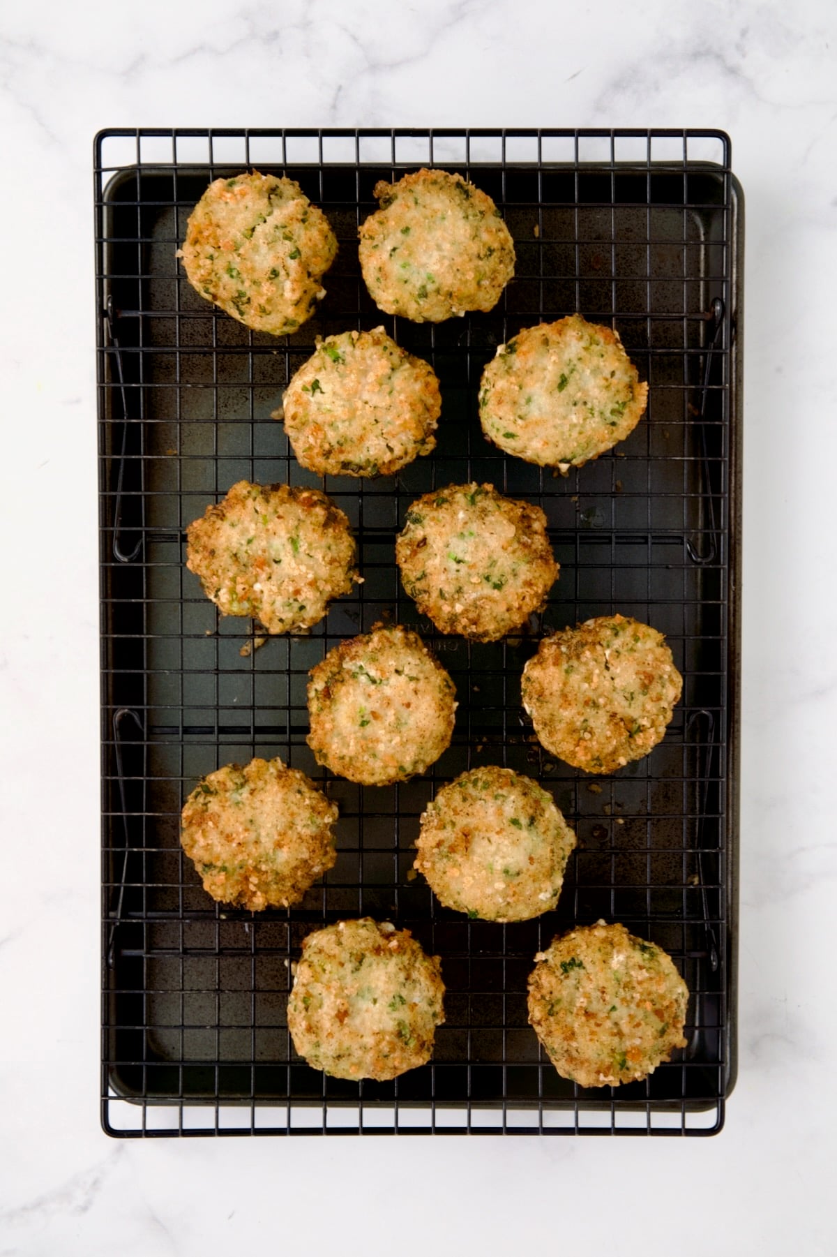 12 cooked shrimp cakes on cooling rack set over a rimmed sheet pan.