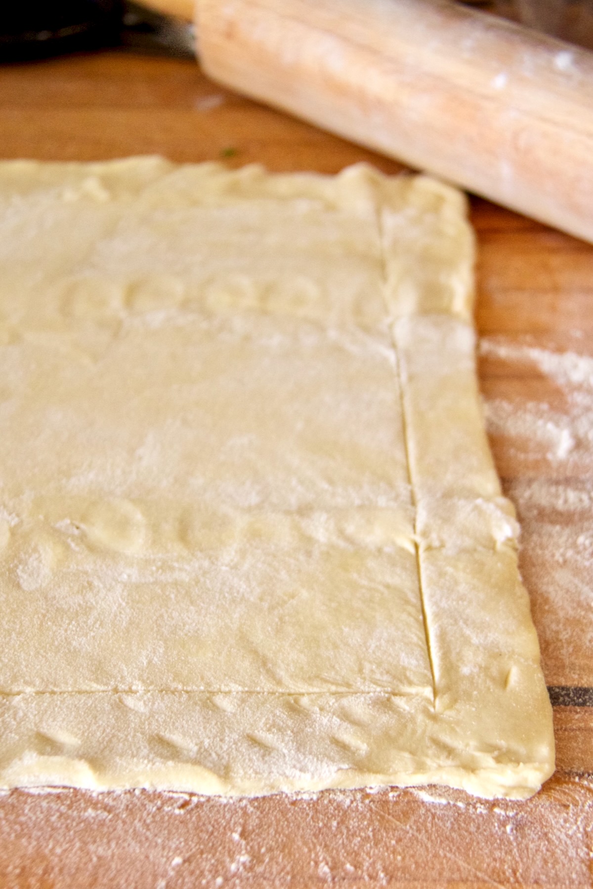 Scored, unbaked puff pastry crust on wood cutting board.