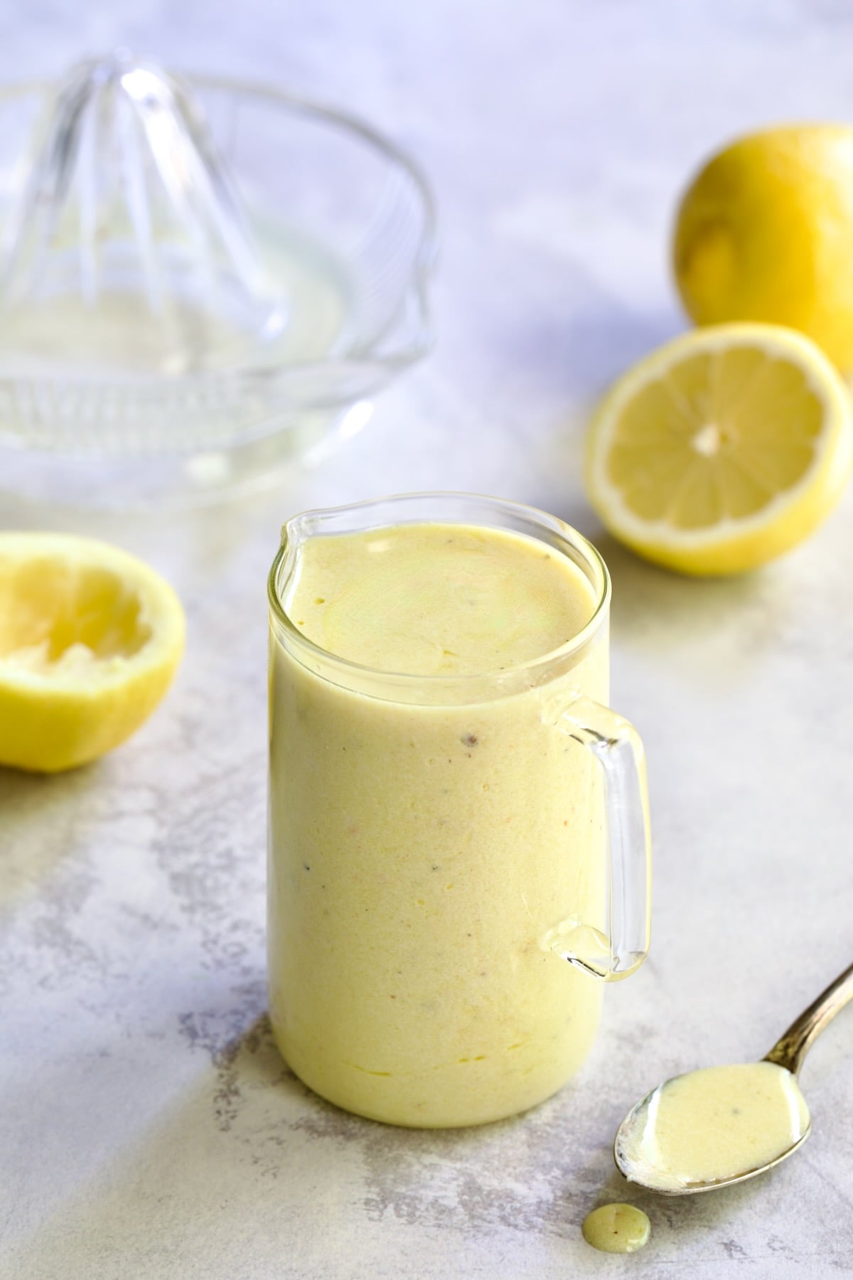 Creamy Lemon Dressing in glass pitcher surrounded by lemon halves with some on a spoon.