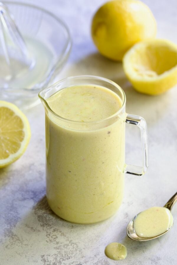 Creamy Lemon Dressing in glass pitcher surrounded by lemon halves.