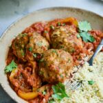 Three Harissa Chicken Meatballs with couscous in earthenware bowl.