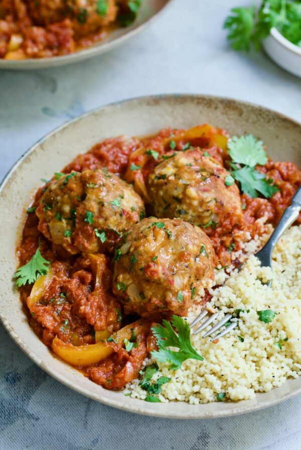 Three Harissa Chicken Meatballs with couscous in earthenware bowl.