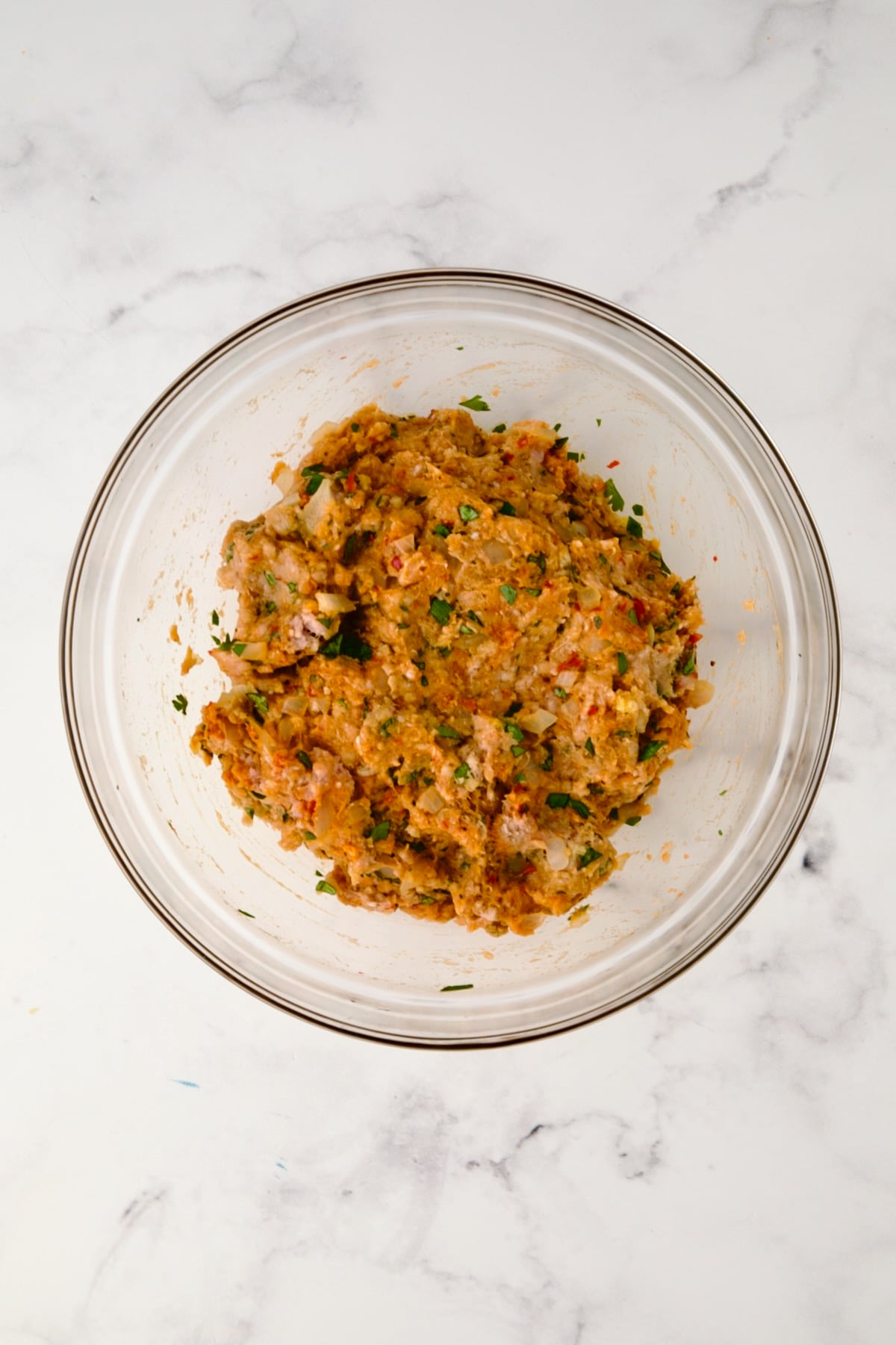 Ingredients for meatballs in glass bowl after being mixed together.