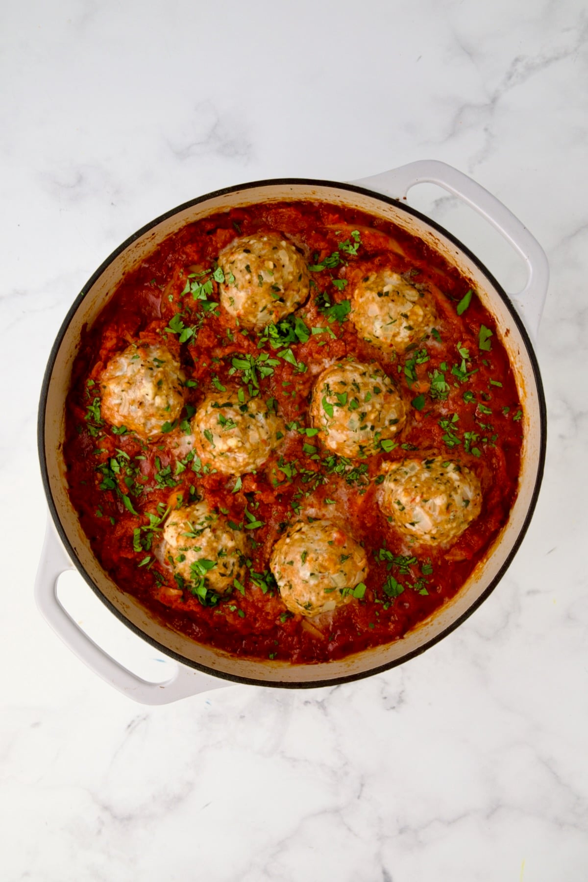Eight cooked Harissa Chicken Meatballs in the sauce in white enamel cast iron skillet.