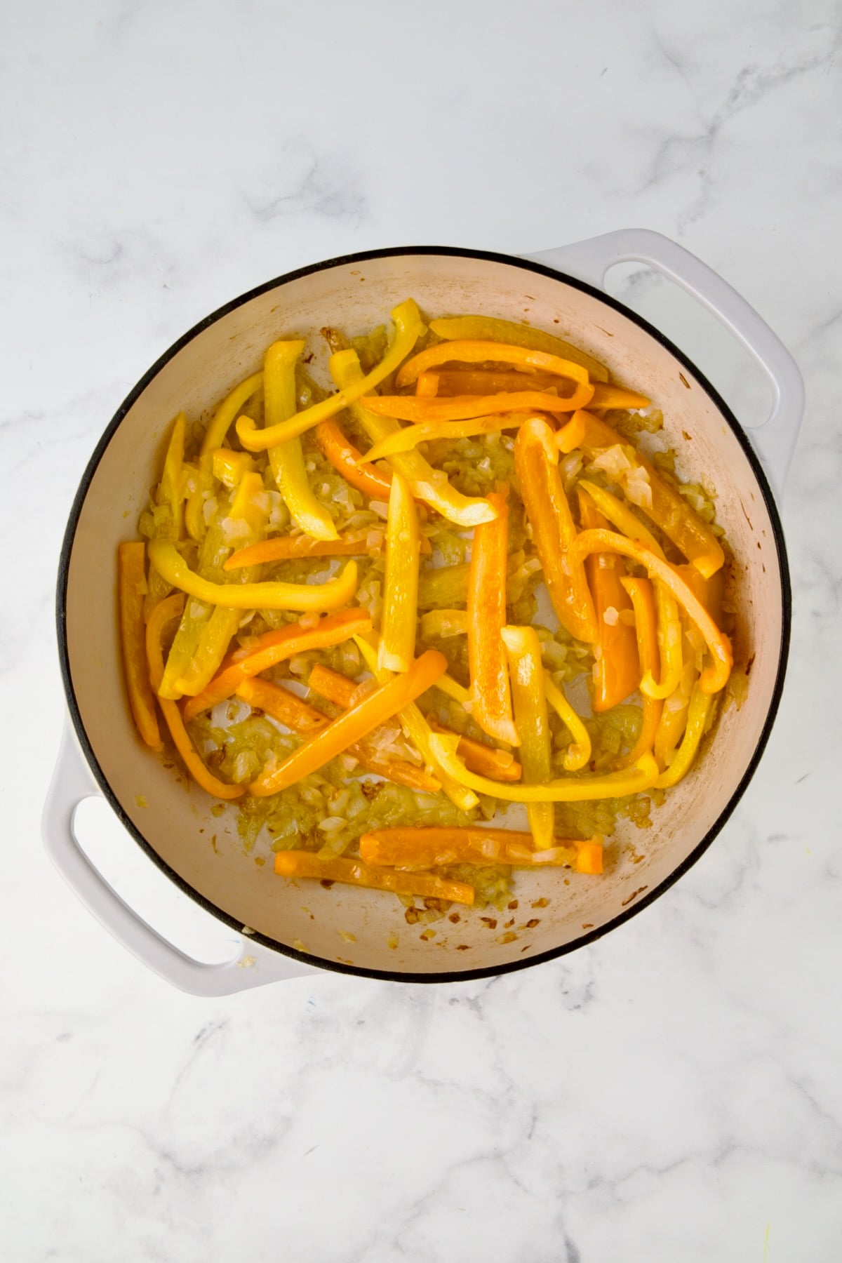 Cooked onions and bell peppers in white enamel cast iron skillet.