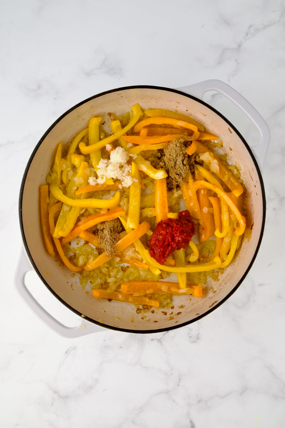 Cooked onions and bell peppers in white enamel cast iron skillet with garlic, cumin, coriander and harissa added.