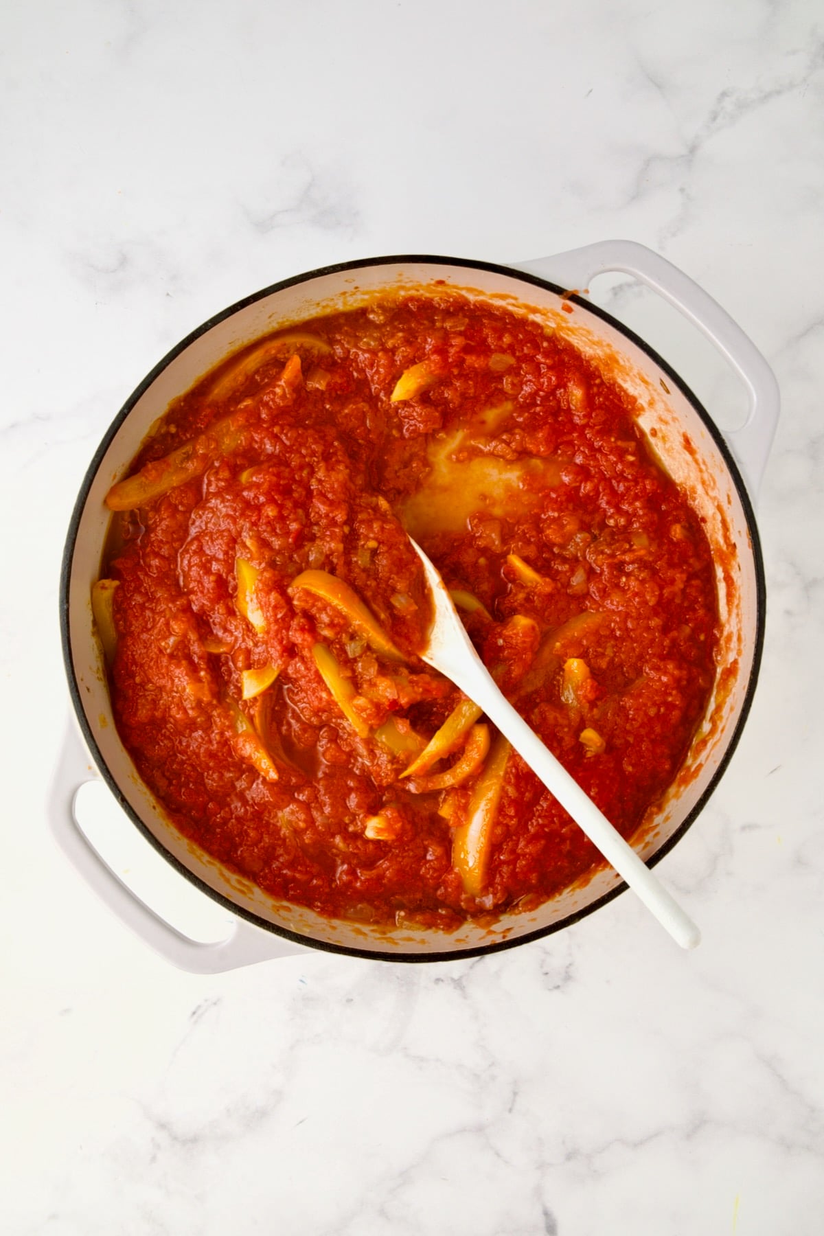 Crushed tomatoes added to onions, bell peppers and spics in white enamel cast iron skillet.