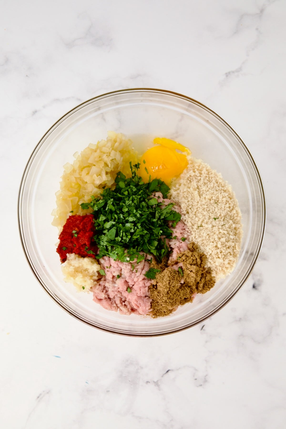 Ingredients for meatballs in glass bowl before being mixed together.