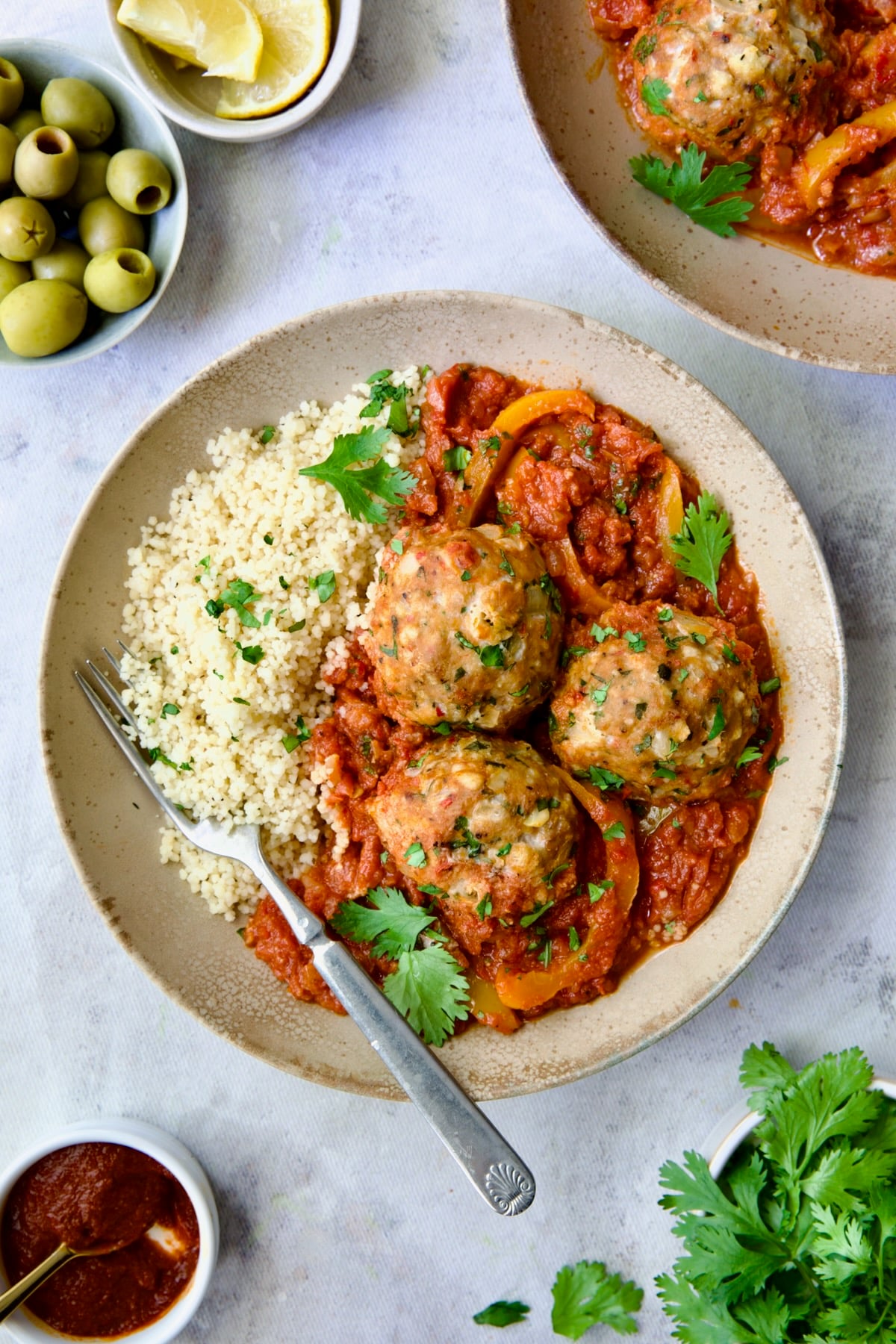 Three Harissa Chicken Meatballs with couscous in earthenware bowl.