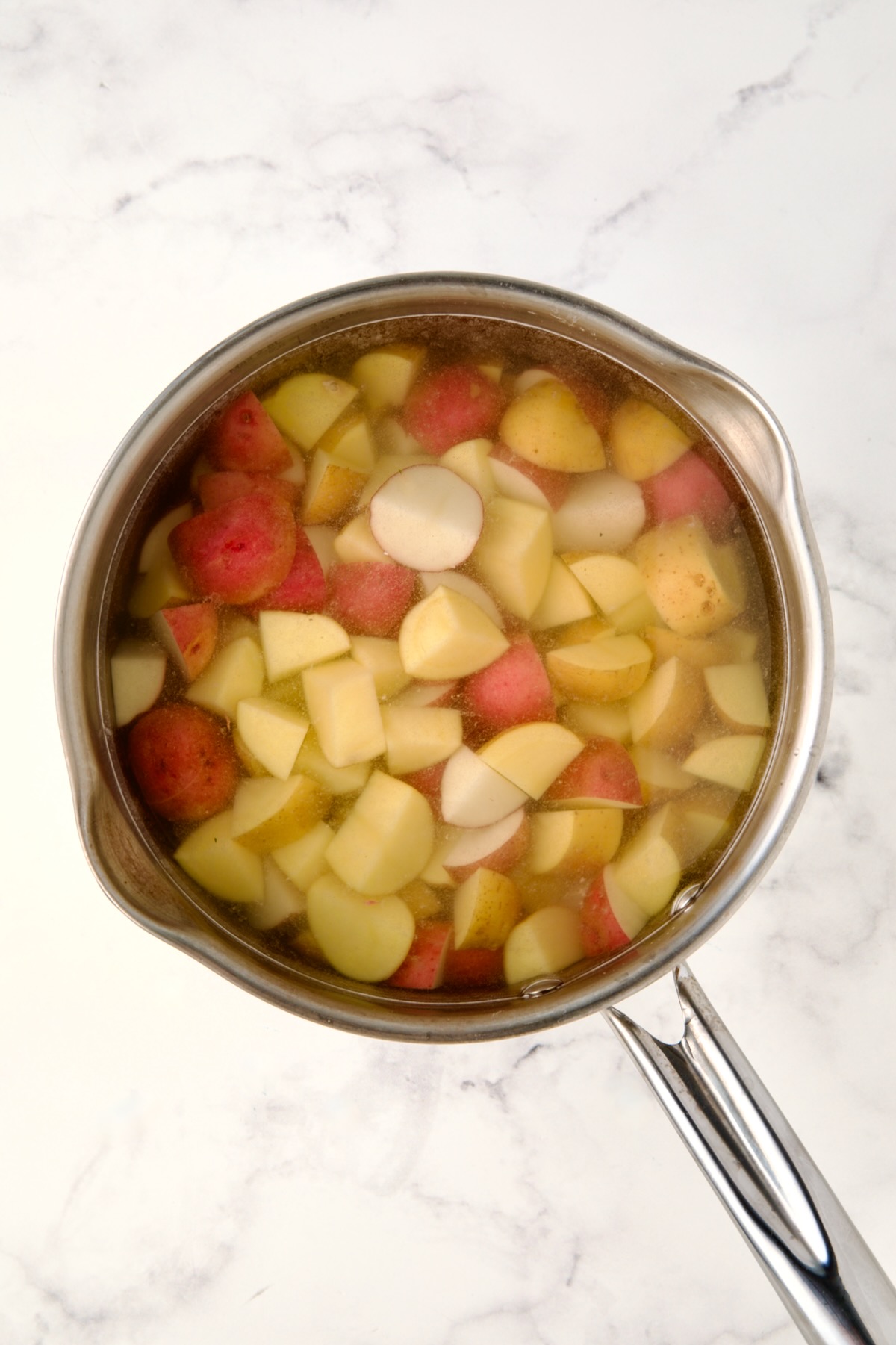 Cubed red and yellow potatoes in water in saucepan.