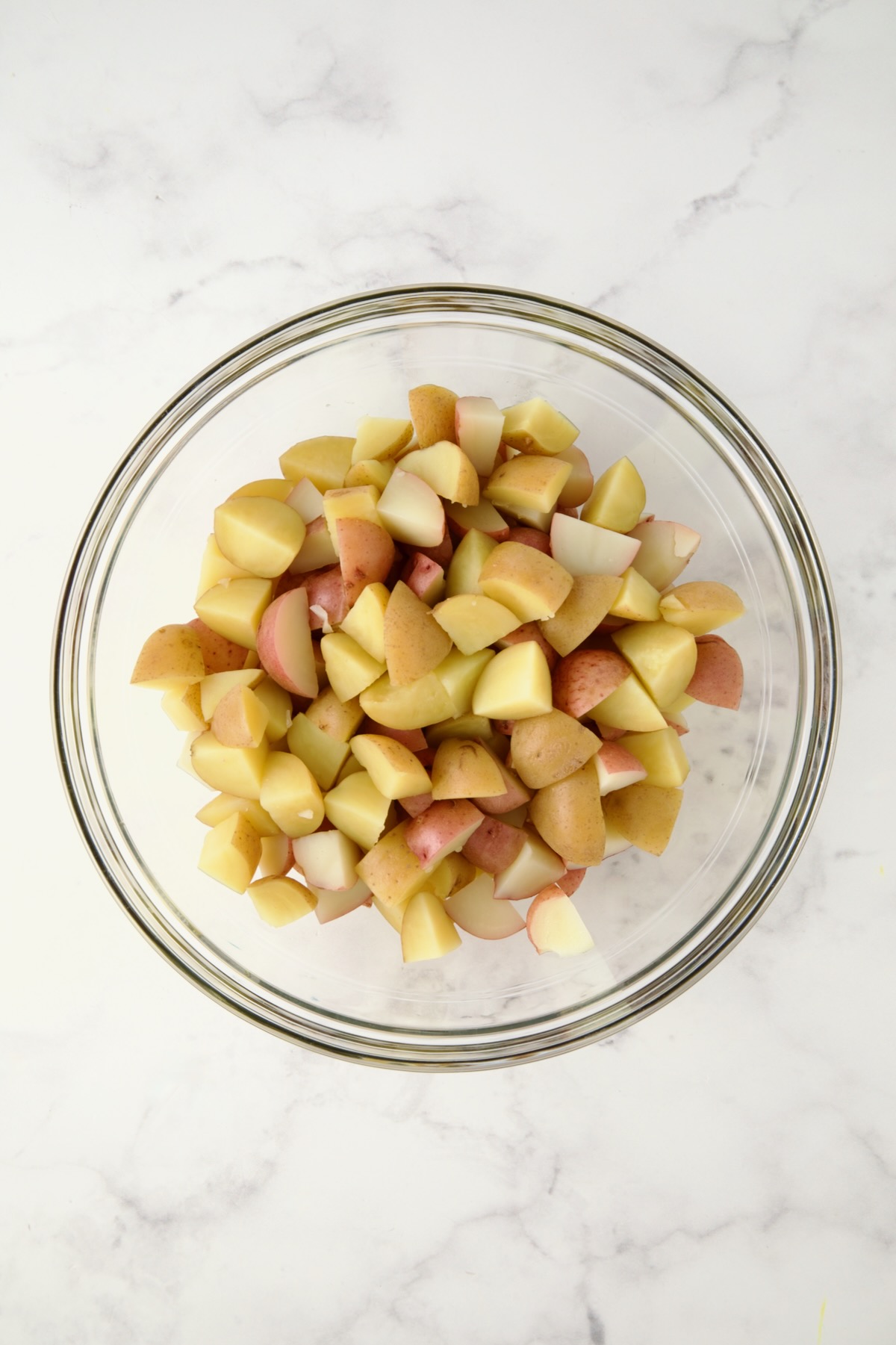 Cubed cooked red and yellow potatoes in glass bowl.