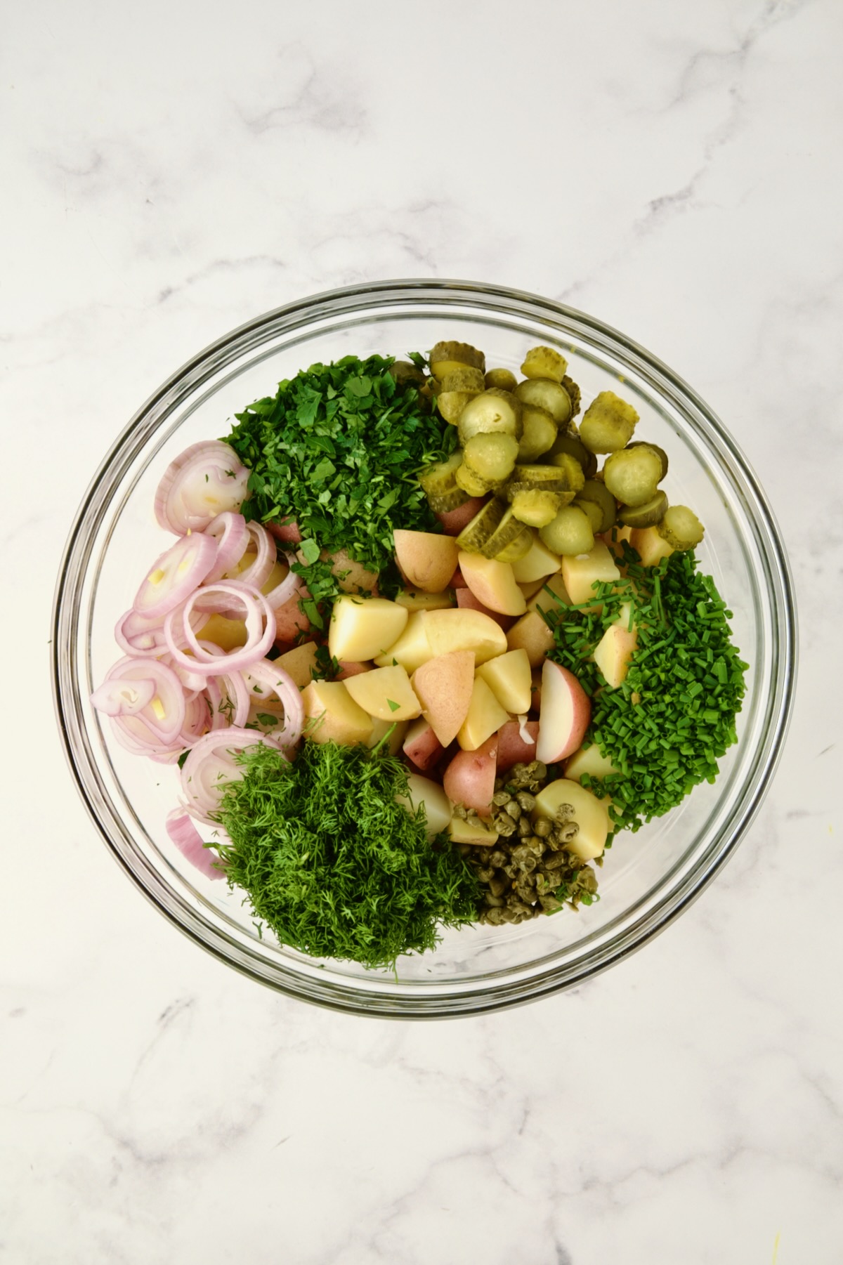 Ingredients for Herb and Vinegar Potato Salad in glass bowl before being mixed together.
