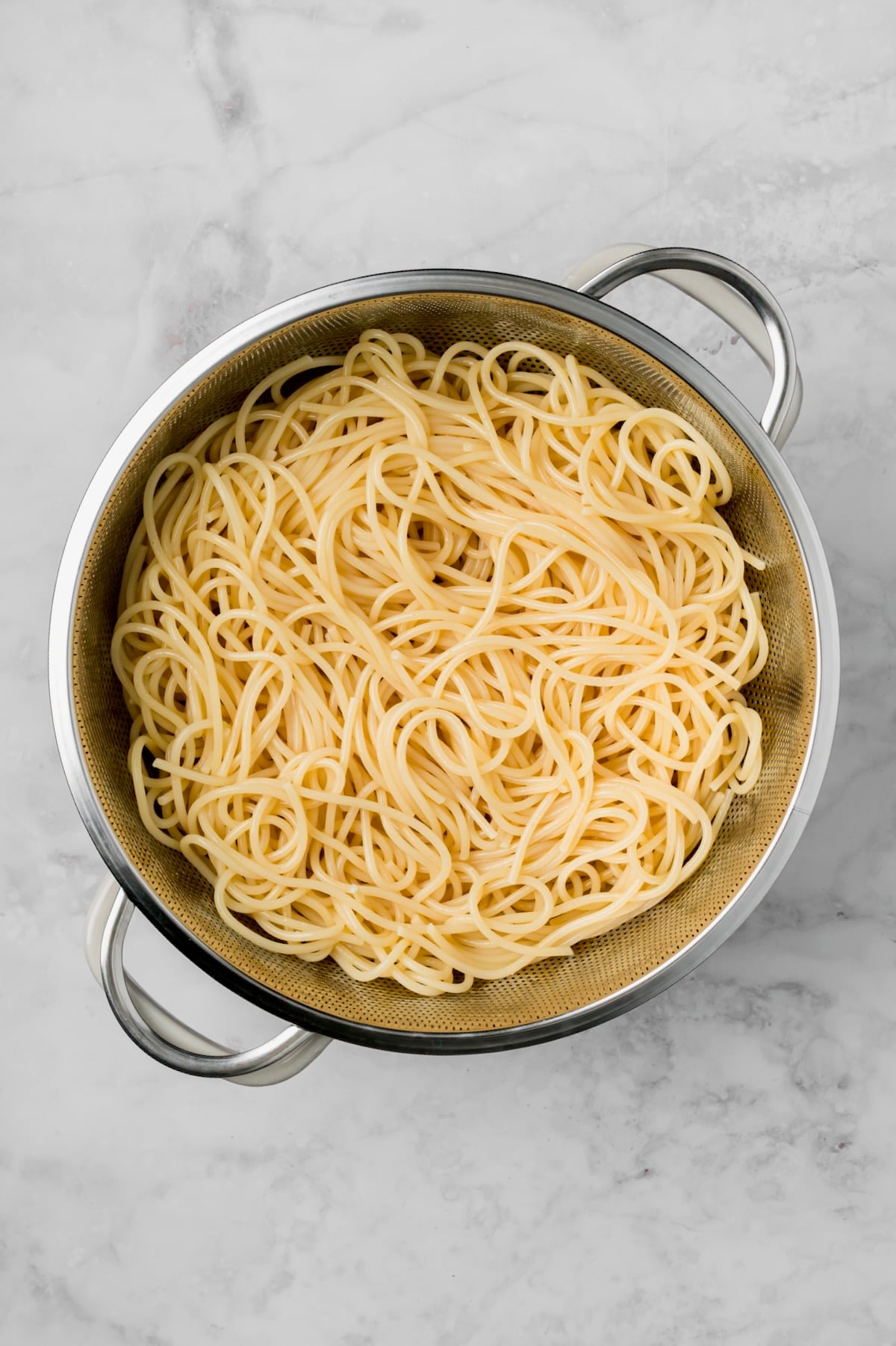 Cooked spaghetti in stainless steel colander.