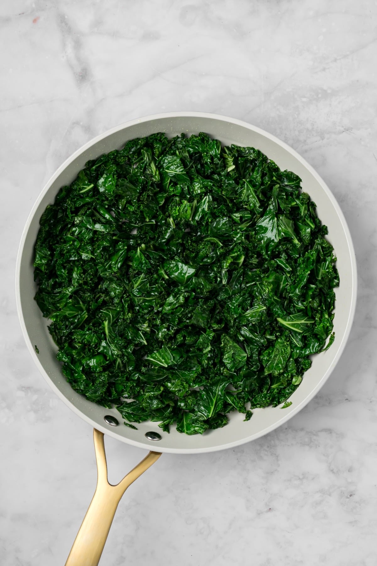 Cooked kale in nonstick white skillet.