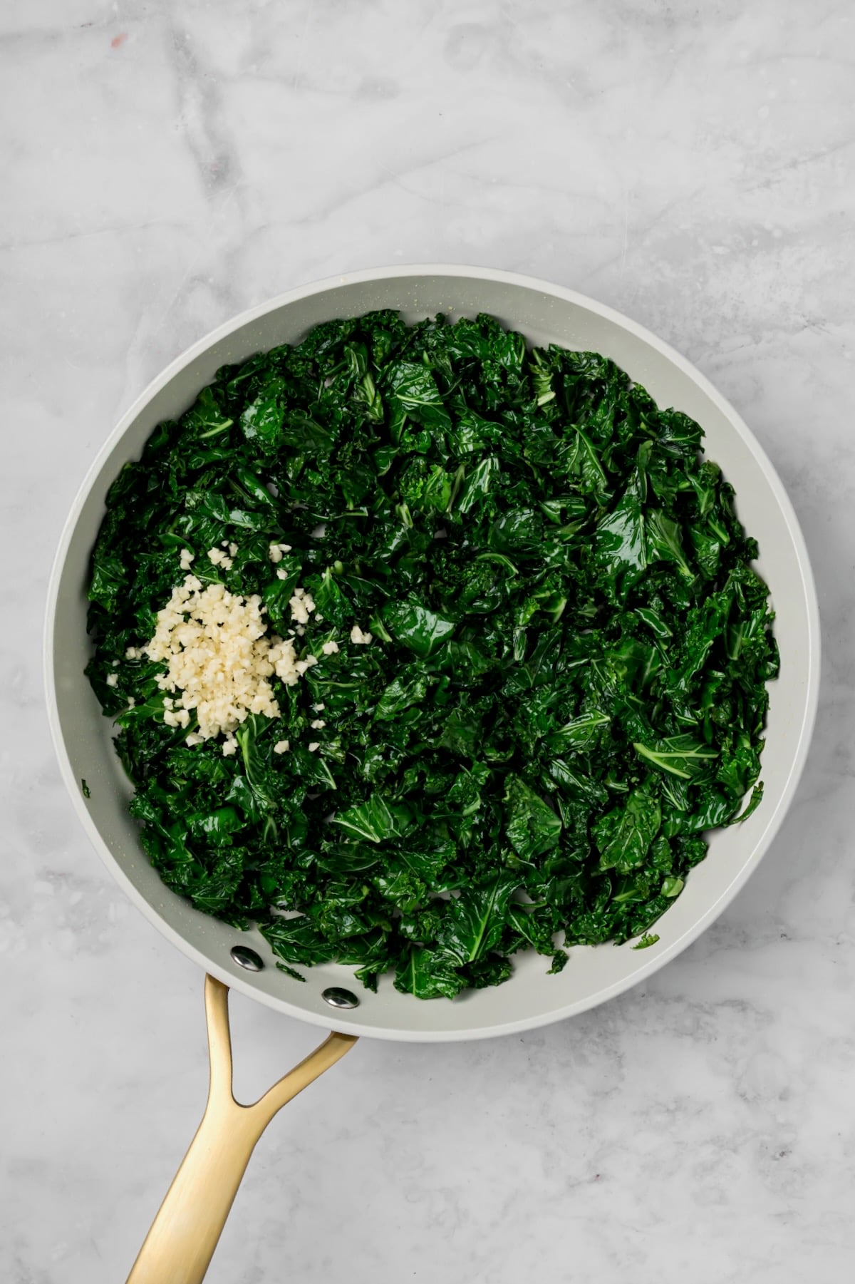 Cooked kale in nonstick white skillet with garlic added.