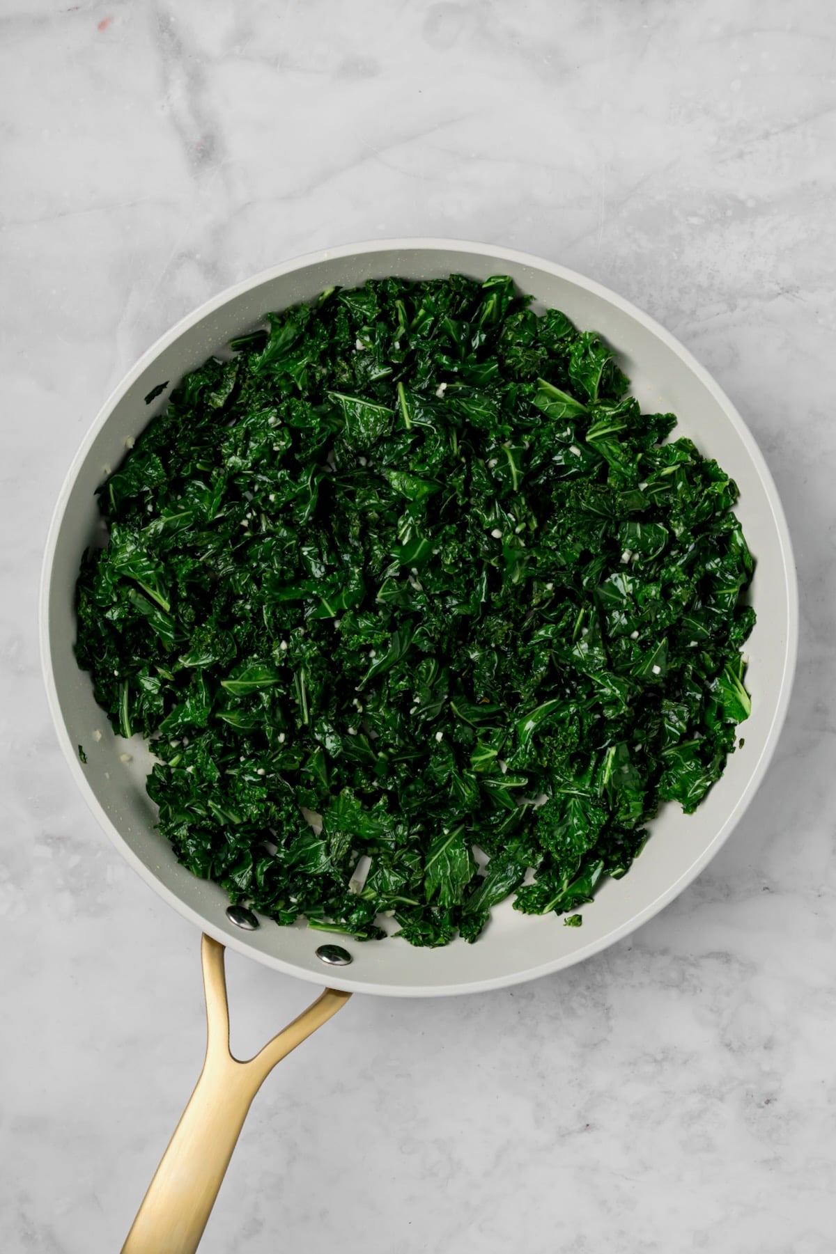 Cooked kale in nonstick white skillet with garlic mixed in.