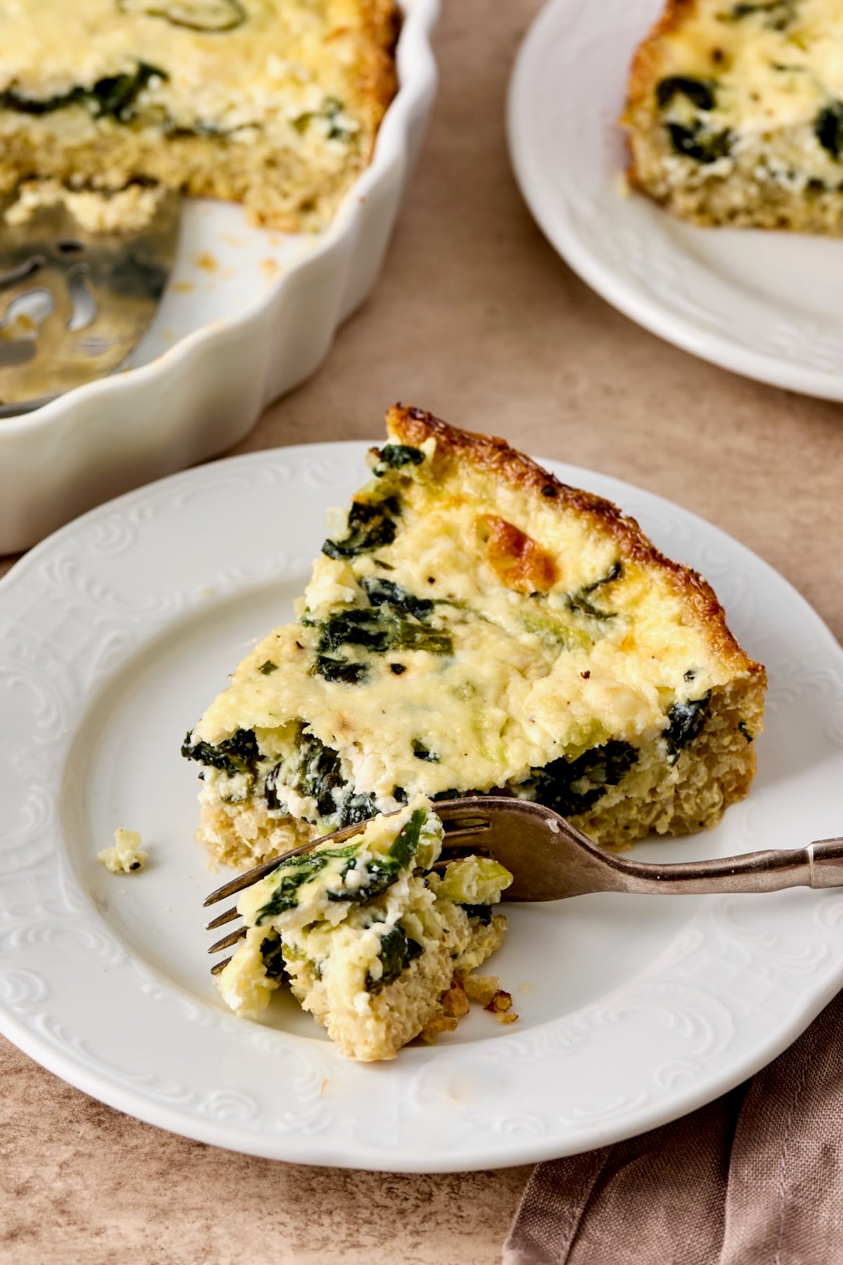 One piece of Spinach Feta Quiche with Quinoa Crust on white plate with fork cutting into it.