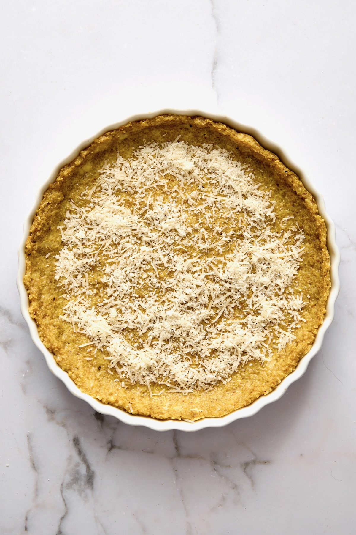 Baked quinoa crust in round white baking dish with Parmesan cheese sprinkled over the top.