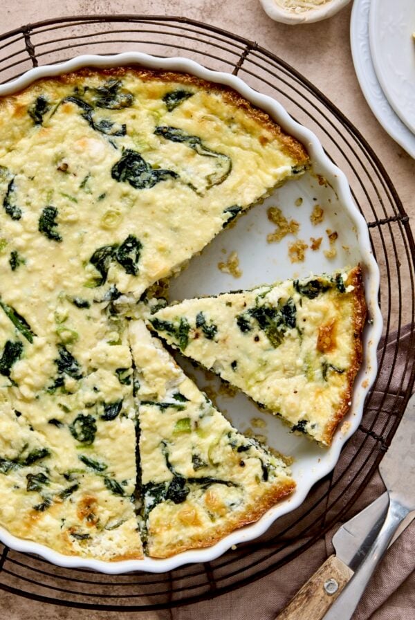 Spinach Feta Quiche with Quinoa Crust in white round baking dish cut into pieces.
