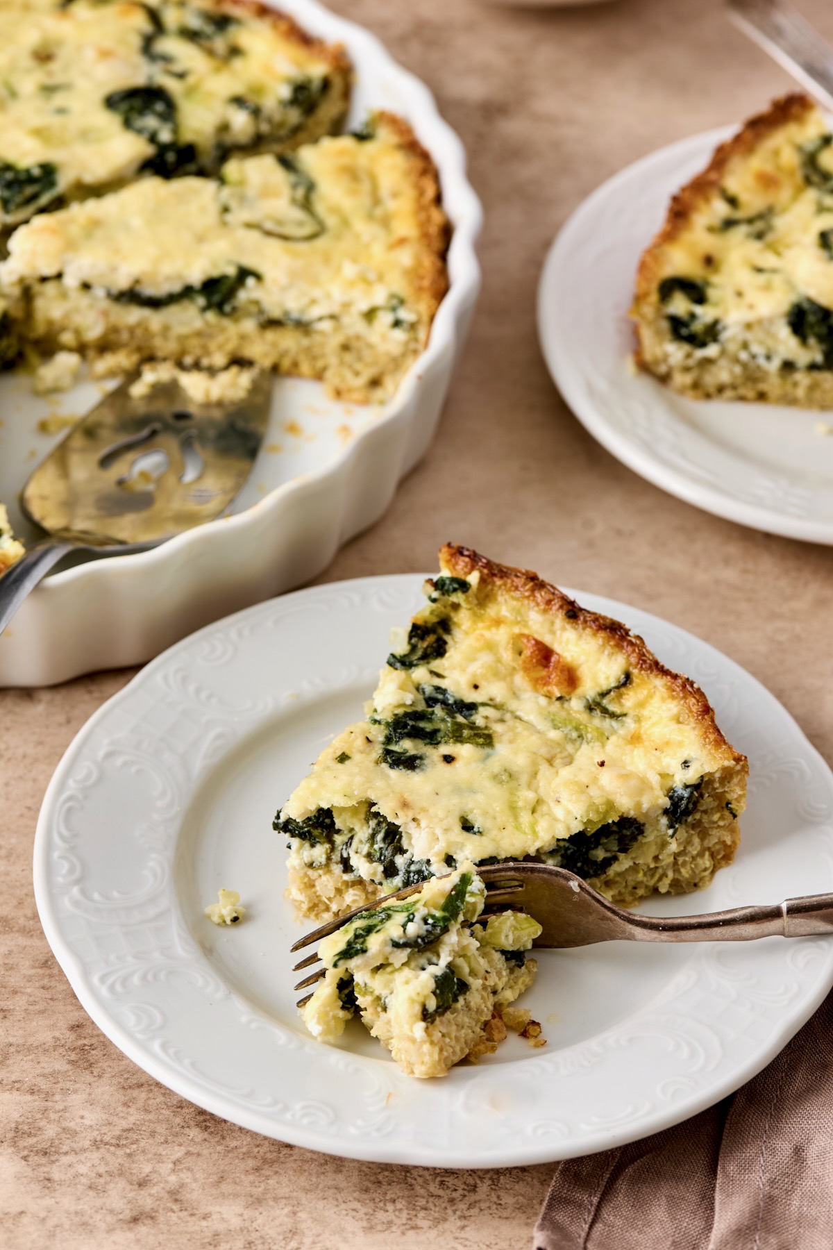 One piece of Spinach Feta Quiche with Quinoa Crust on white plate with fork cutting into it.