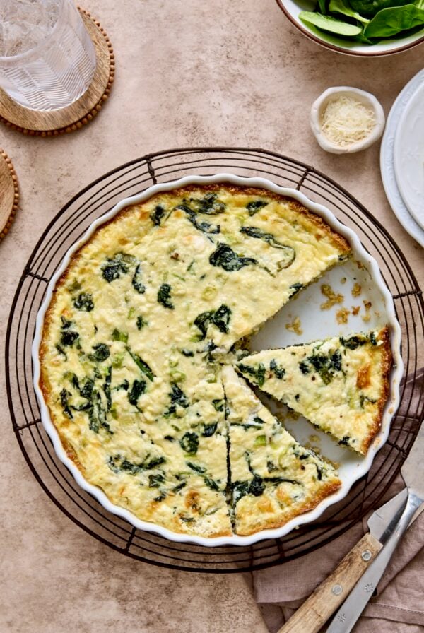 Spinach Feta Quiche with Quinoa Crust in white round baking dish cut into pieces.