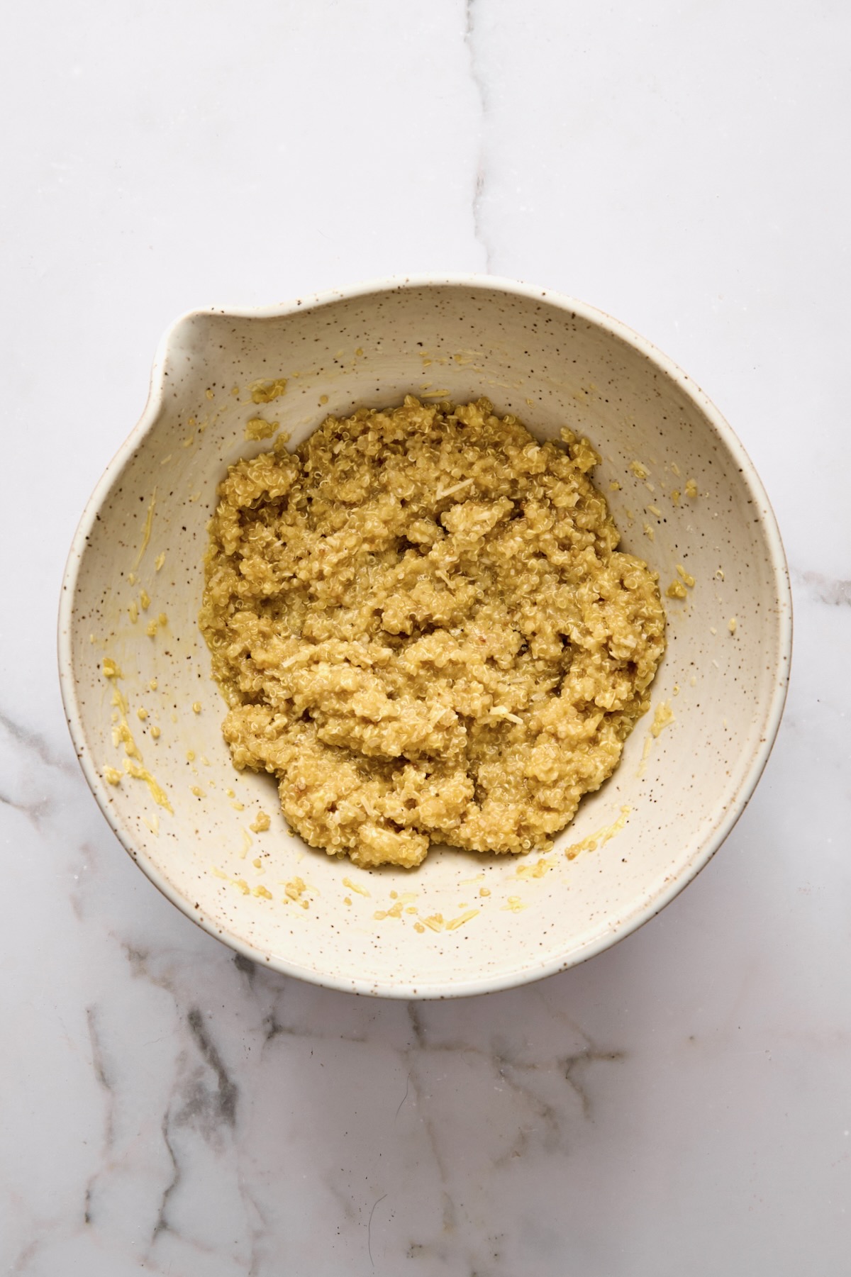 Cooked quinoa, eggs, and cheese combined in mixing bowl.