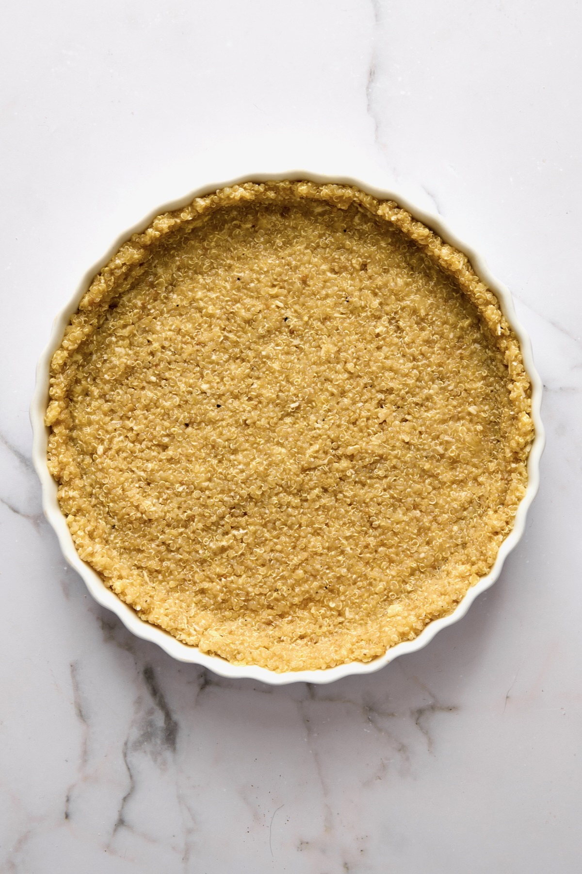 Unbaked quinoa crust in round white baking dish.