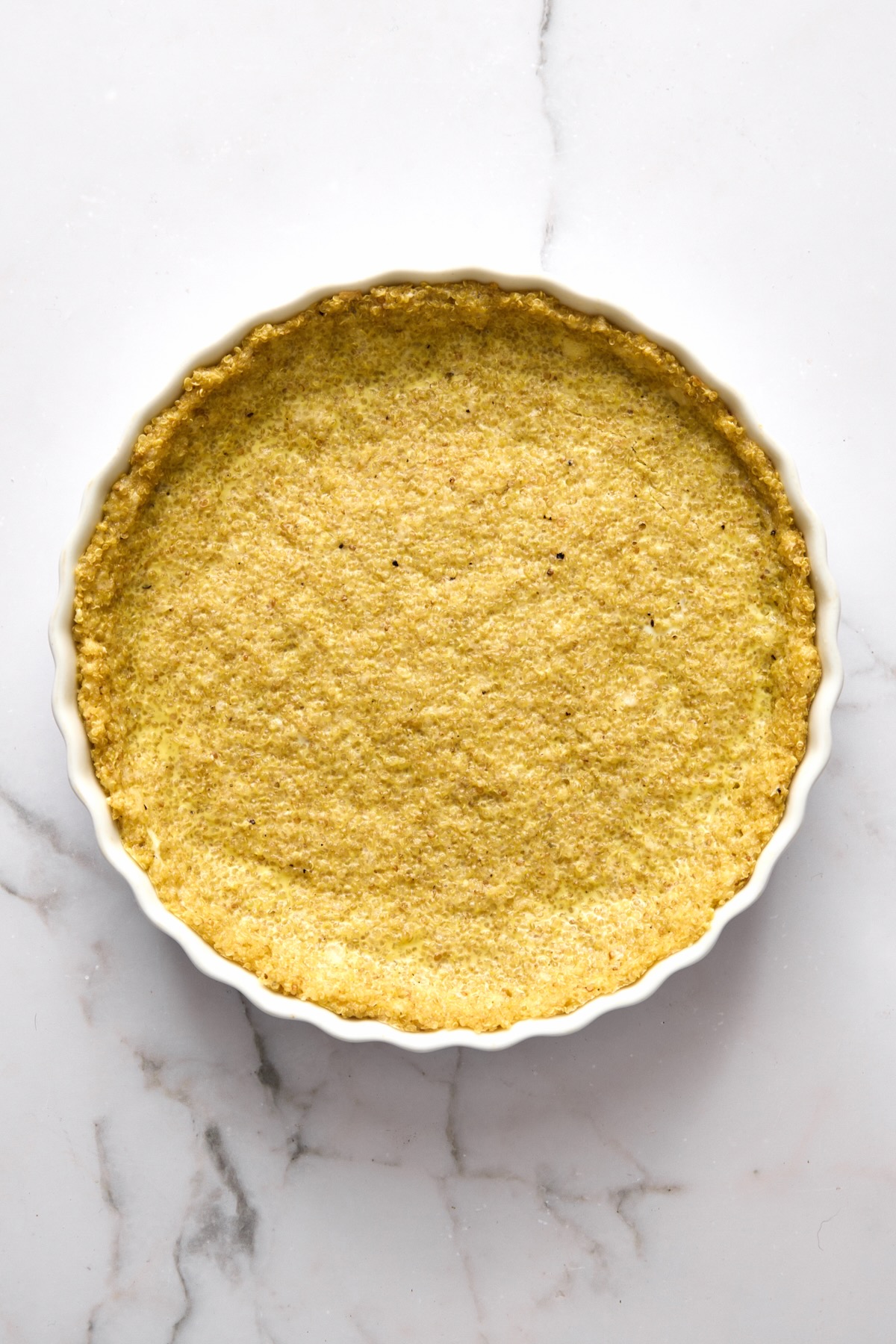 Baked quinoa crust in round white baking dish.