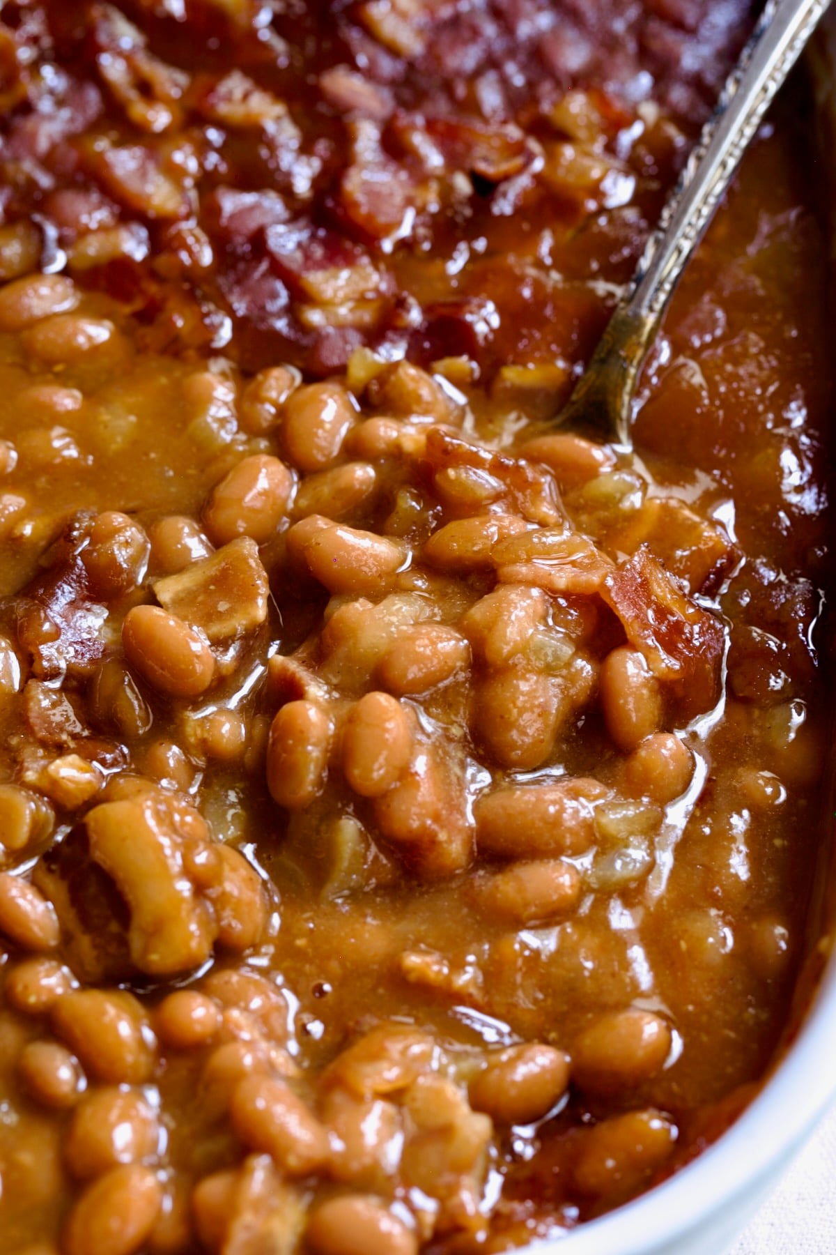 Best Canned Baked Beans Recipe in oval white baking dish with serving spoon.