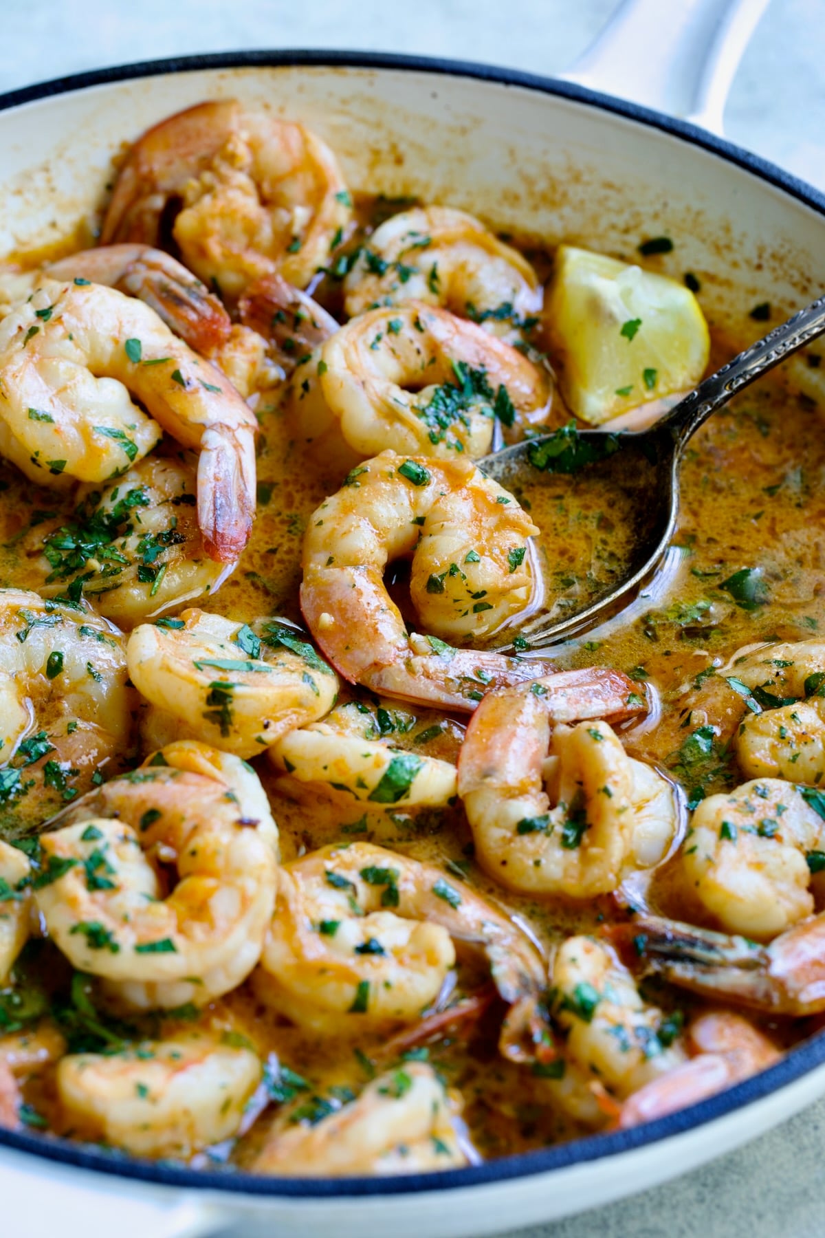 Cajun Butter Shrimp in white enamel cast iron skillet with spoon lifting up one shrimp.