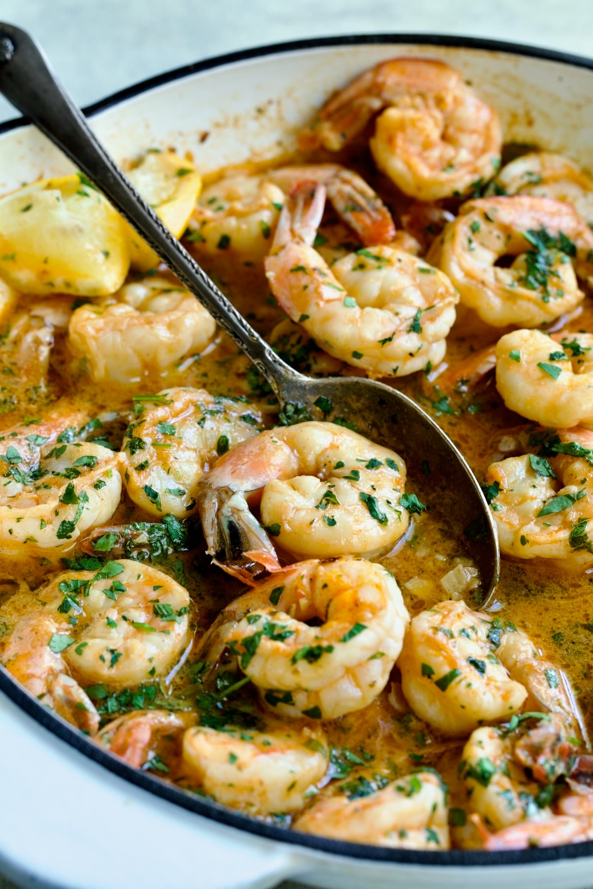 Cajun Butter Shrimp in white enamel cast iron skillet with spoon picking up a shrimp.