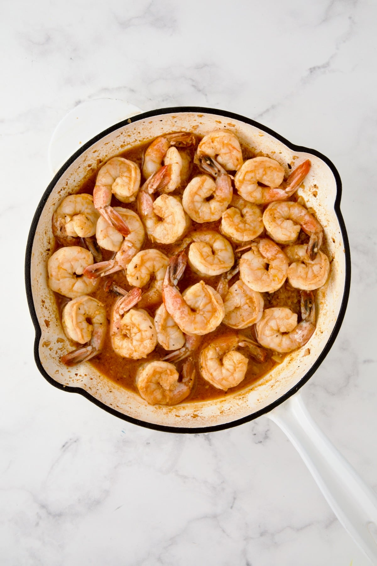Shrimp added to reduced sauce in white enamel cast iron skillet.