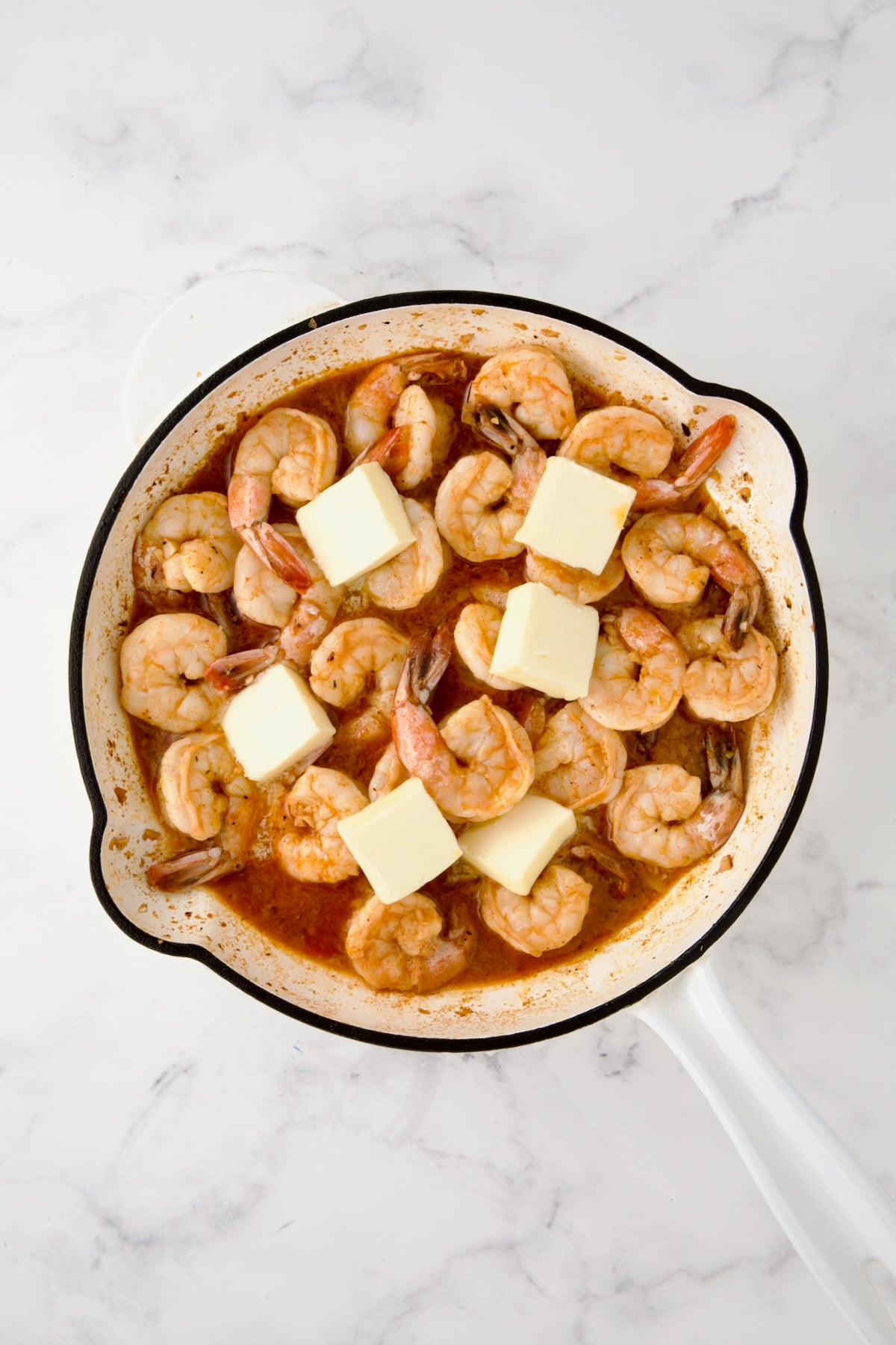 Butter added to cooked shrimp in white enamel cast iron skillet.