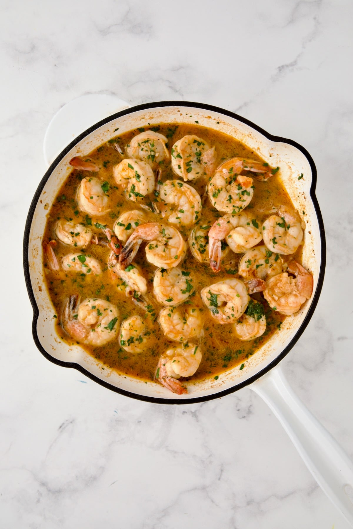 Butter fully melted over cooked shrimp in white enamel cast iron skillet with parsley sprinkled over.