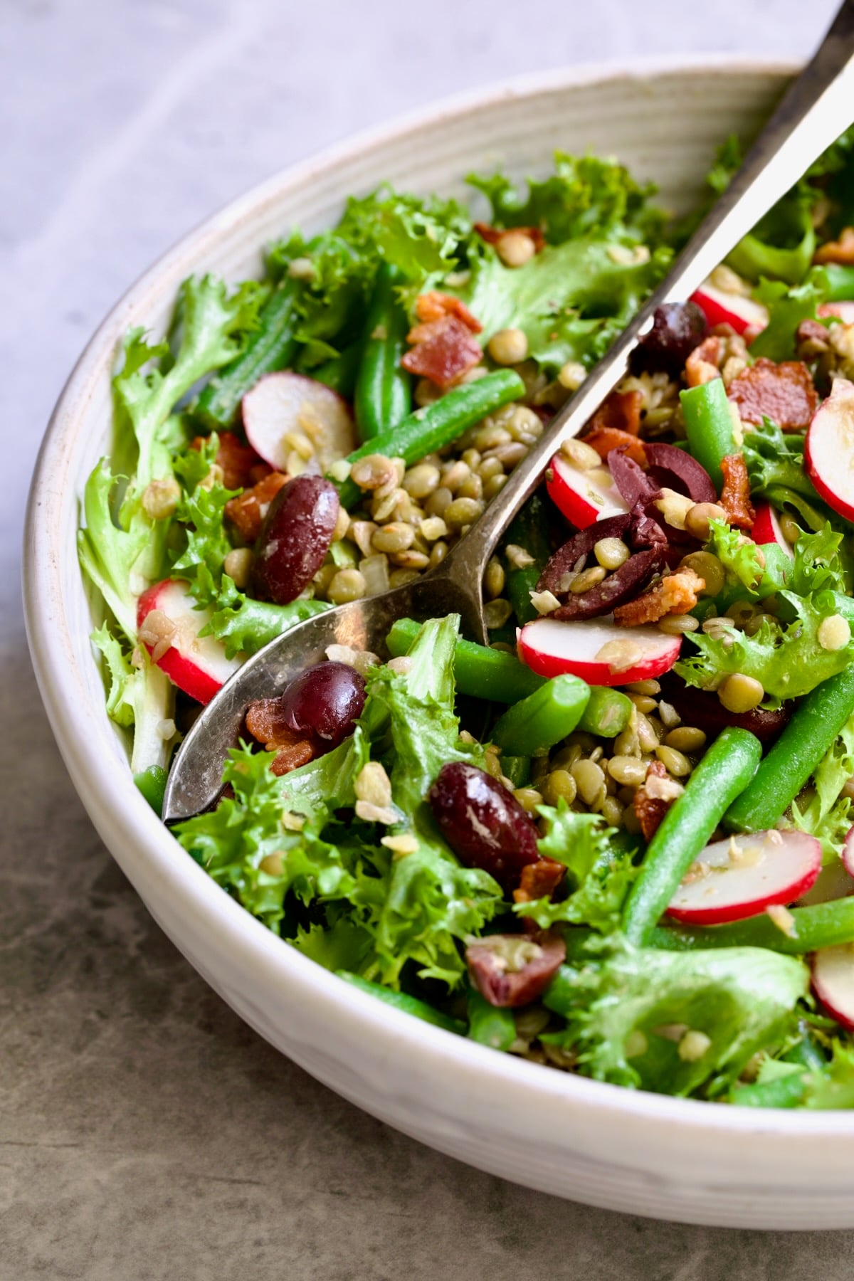 French Lentil Salad in white serving bowl with serving utensils.