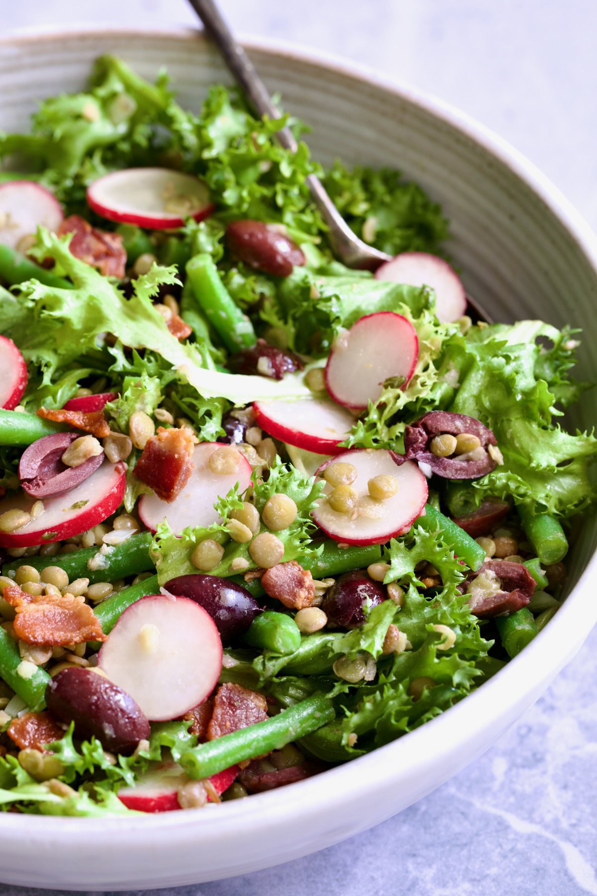 French Lentil Salad in white serving bowl with serving utensils.