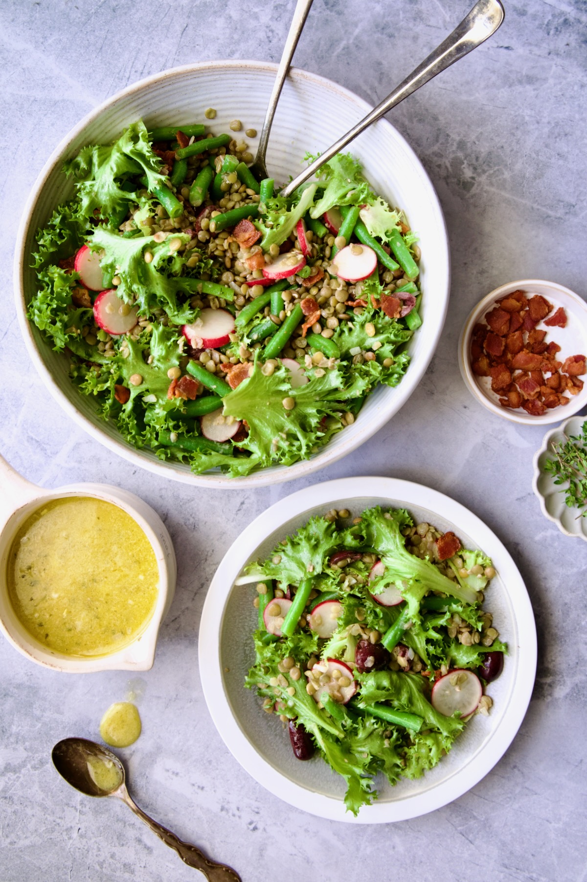 French Lentil Salad over lettuce in white serving bowl with serving utensils with some served up on a white plate.