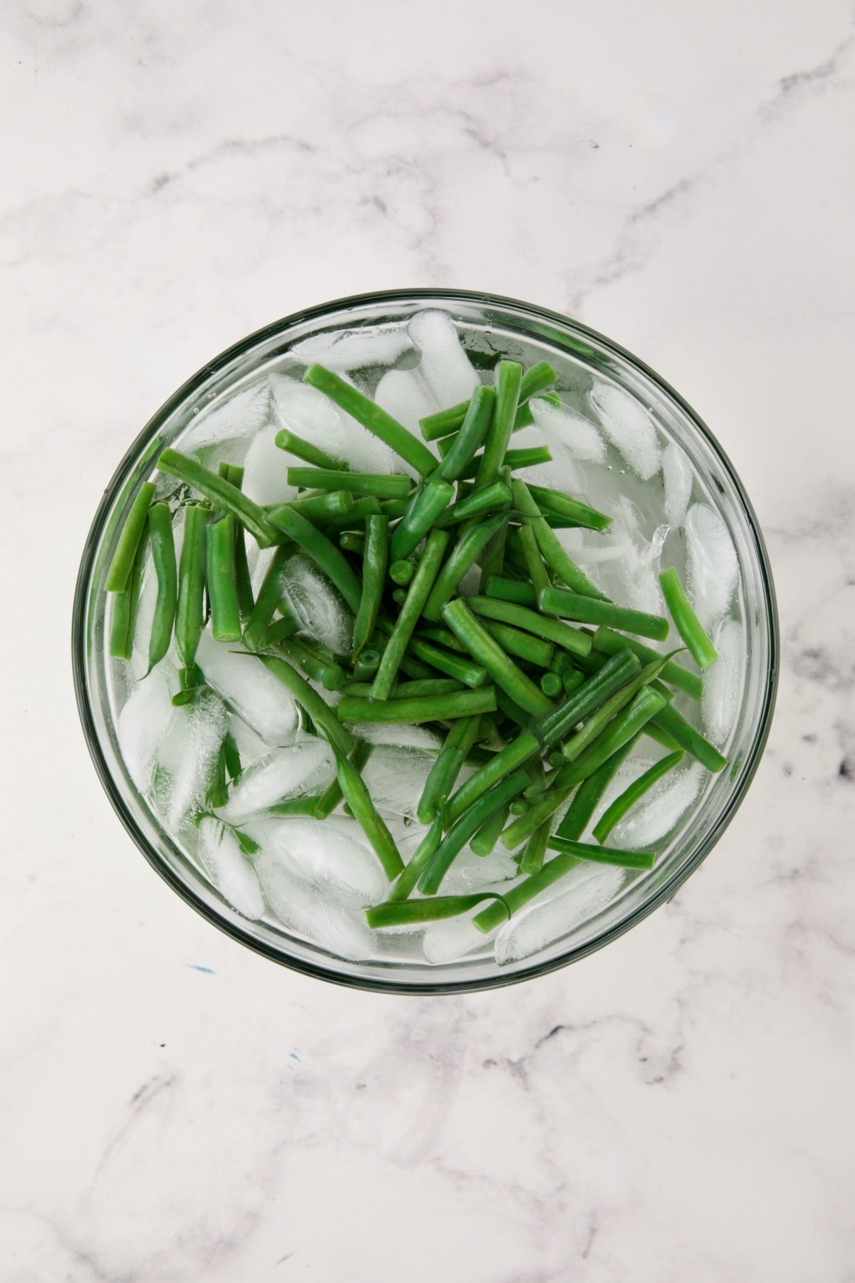 Blanched green beans in ice bath in glass bowl.